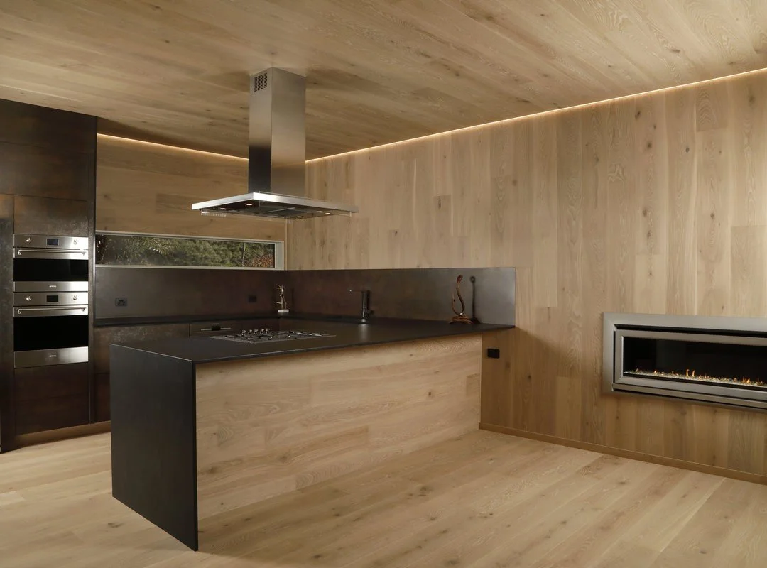 Modern kitchen with wooden walls and ceiling, black countertops, stainless steel appliances, and a built-in fireplace on the wall.