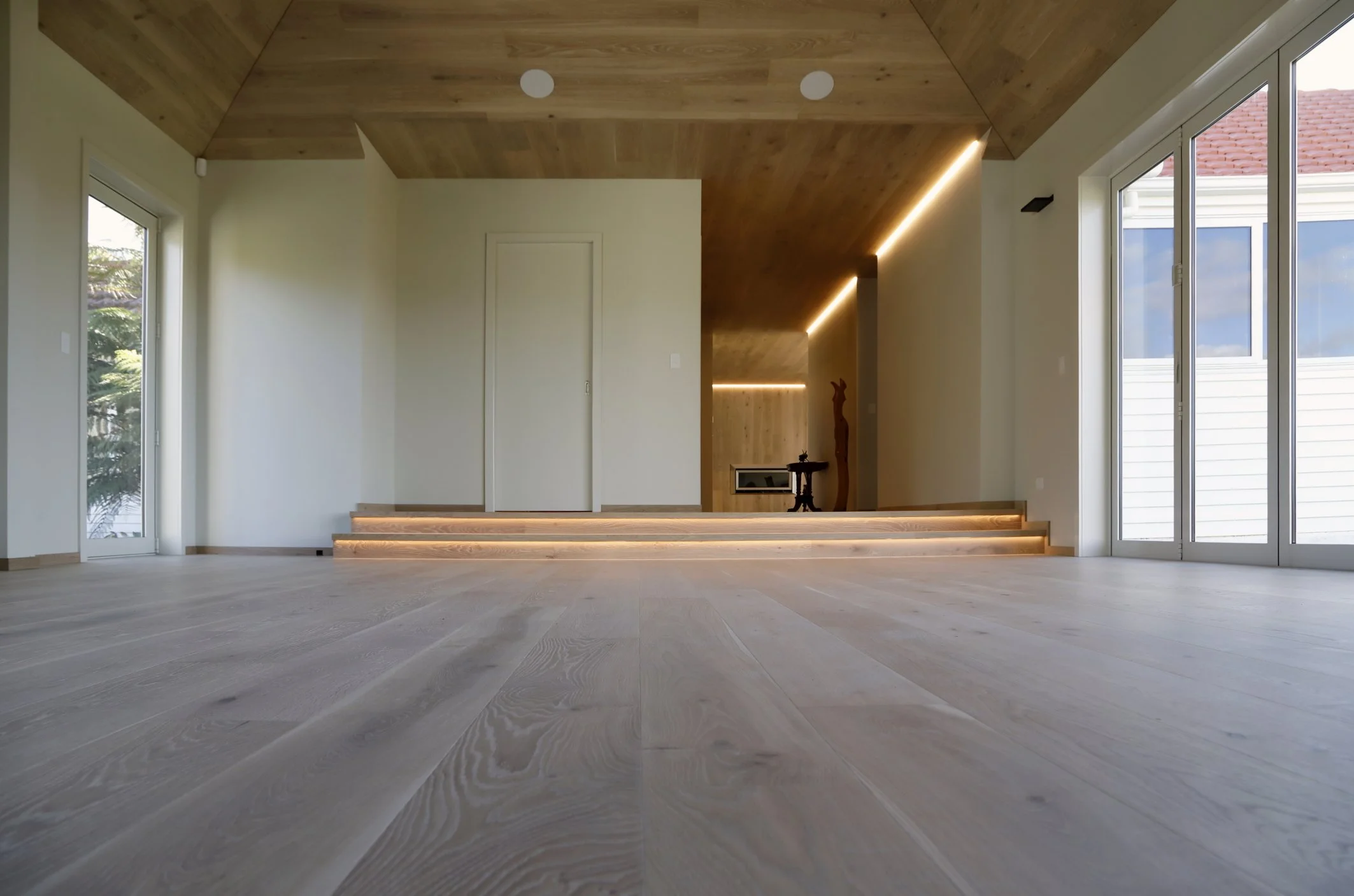 Empty room with wooden ceiling, large windows, and stairs with LED strip lighting.