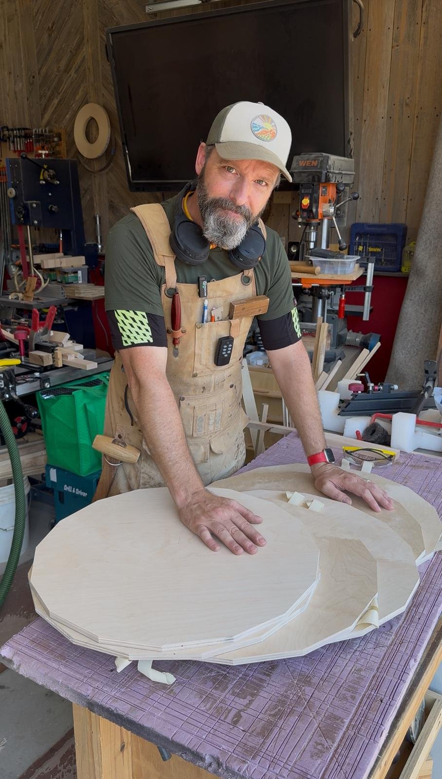 A man in a woodworking shop standing behind a large, intricately cut piece of wood work table with his hands resting on it.
