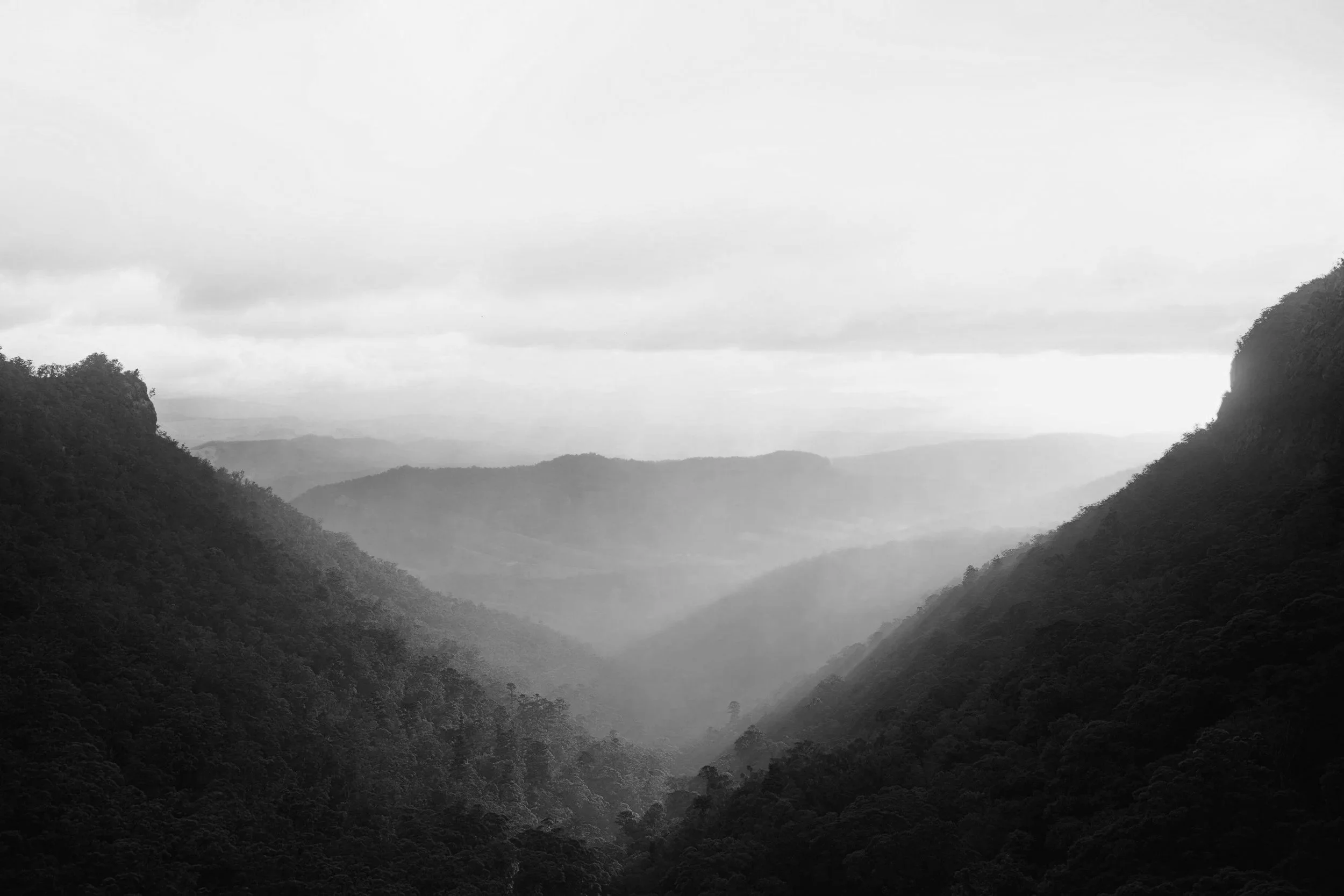 Black and white photograph of a mountain landscape with layers of mountains fading into the distance under a cloudy sky, demonstrating solidity and security.