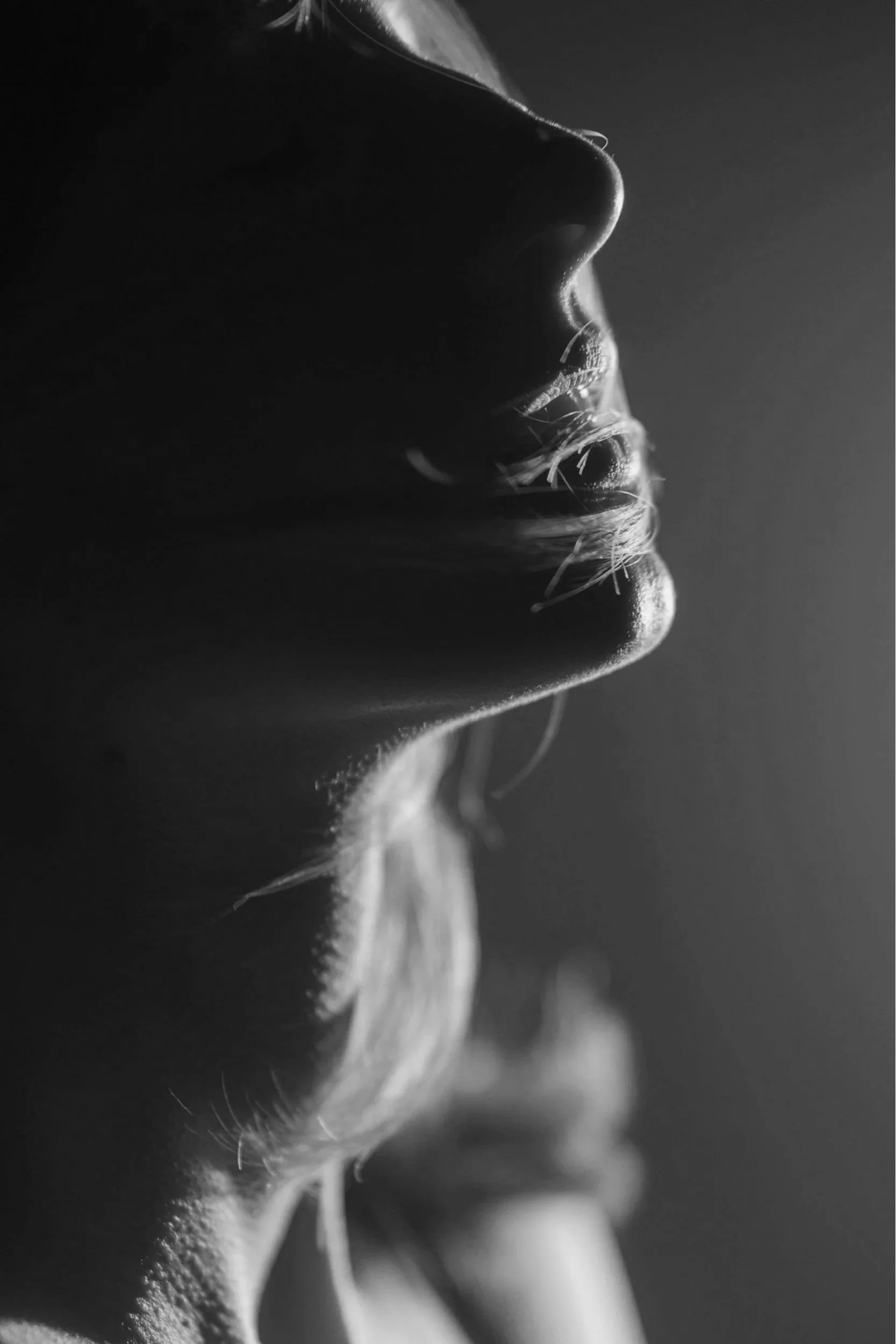 Close-up black and white photo of a woman's profile with lighting highlighting her lips, nose, and chin, demonstrating the concept of breath work.
