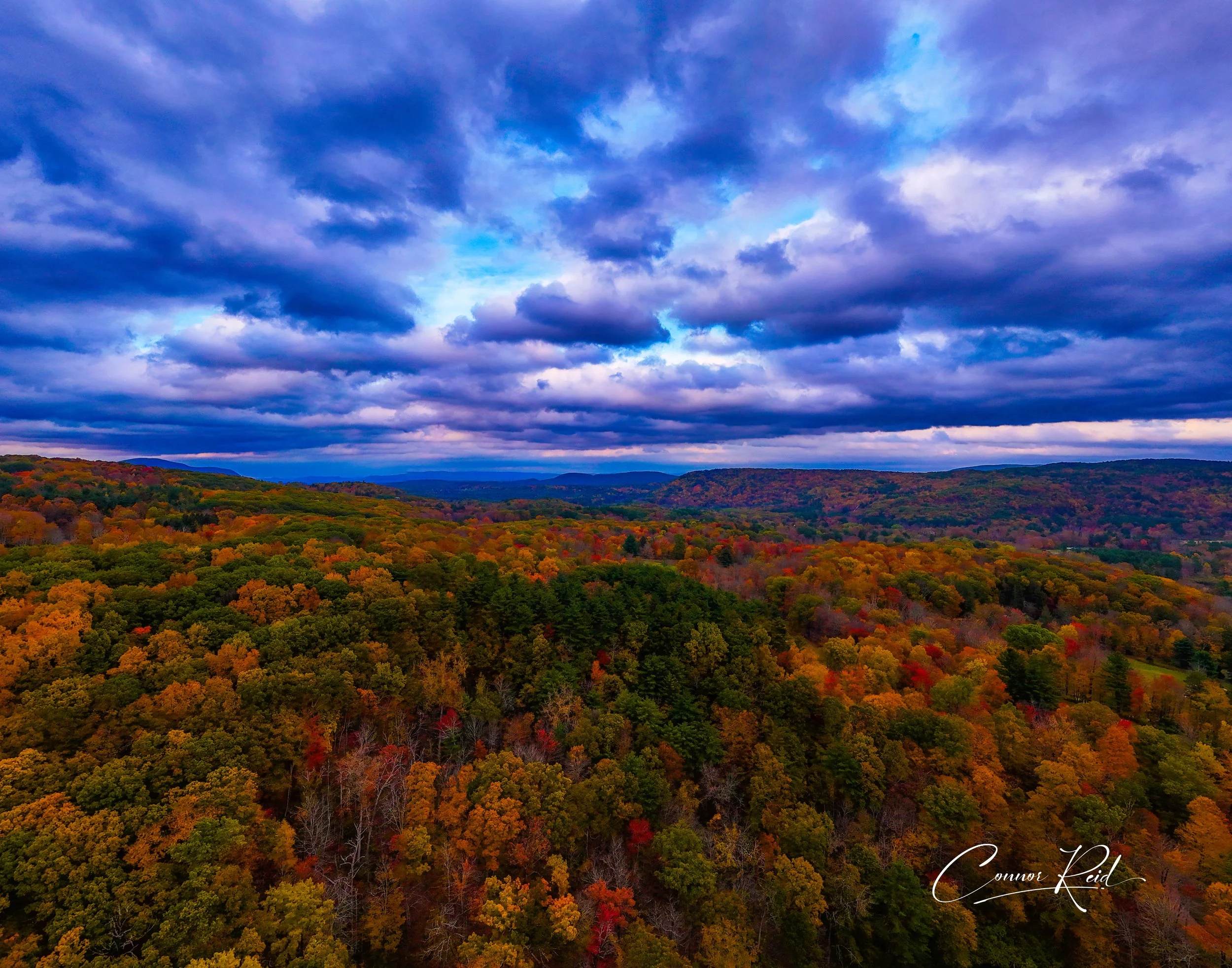 Aerial view of autumn forest with colorful trees under a dramatic blue sky with clouds.