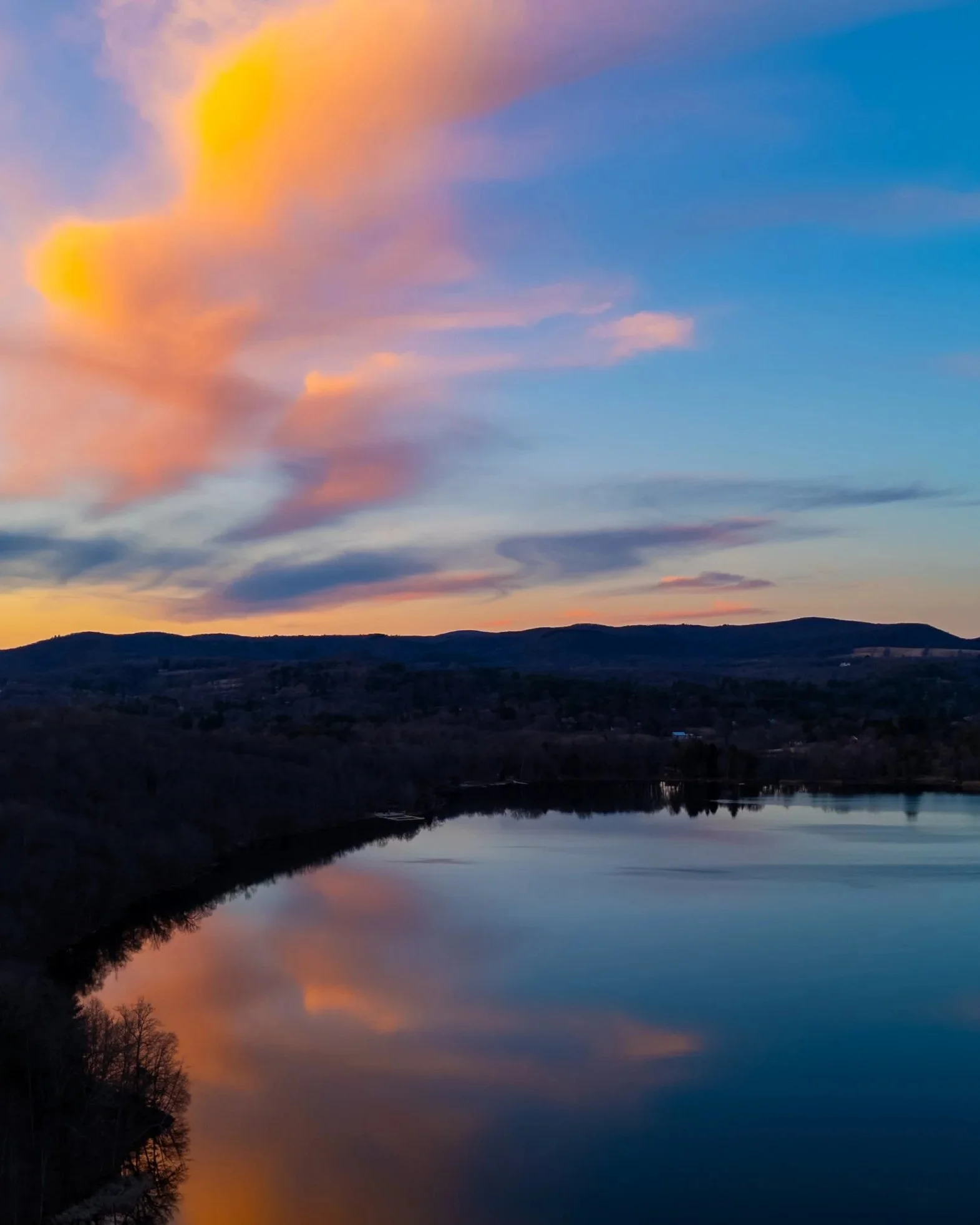 A scenic view of a sunset with colorful clouds over a calm lake and distant hills.