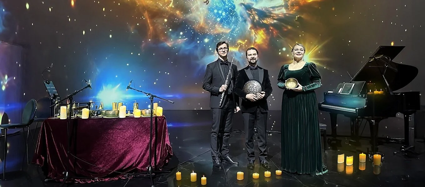 Three musicians standing on stage with candles, a grand piano, and a vibrant cosmic background.