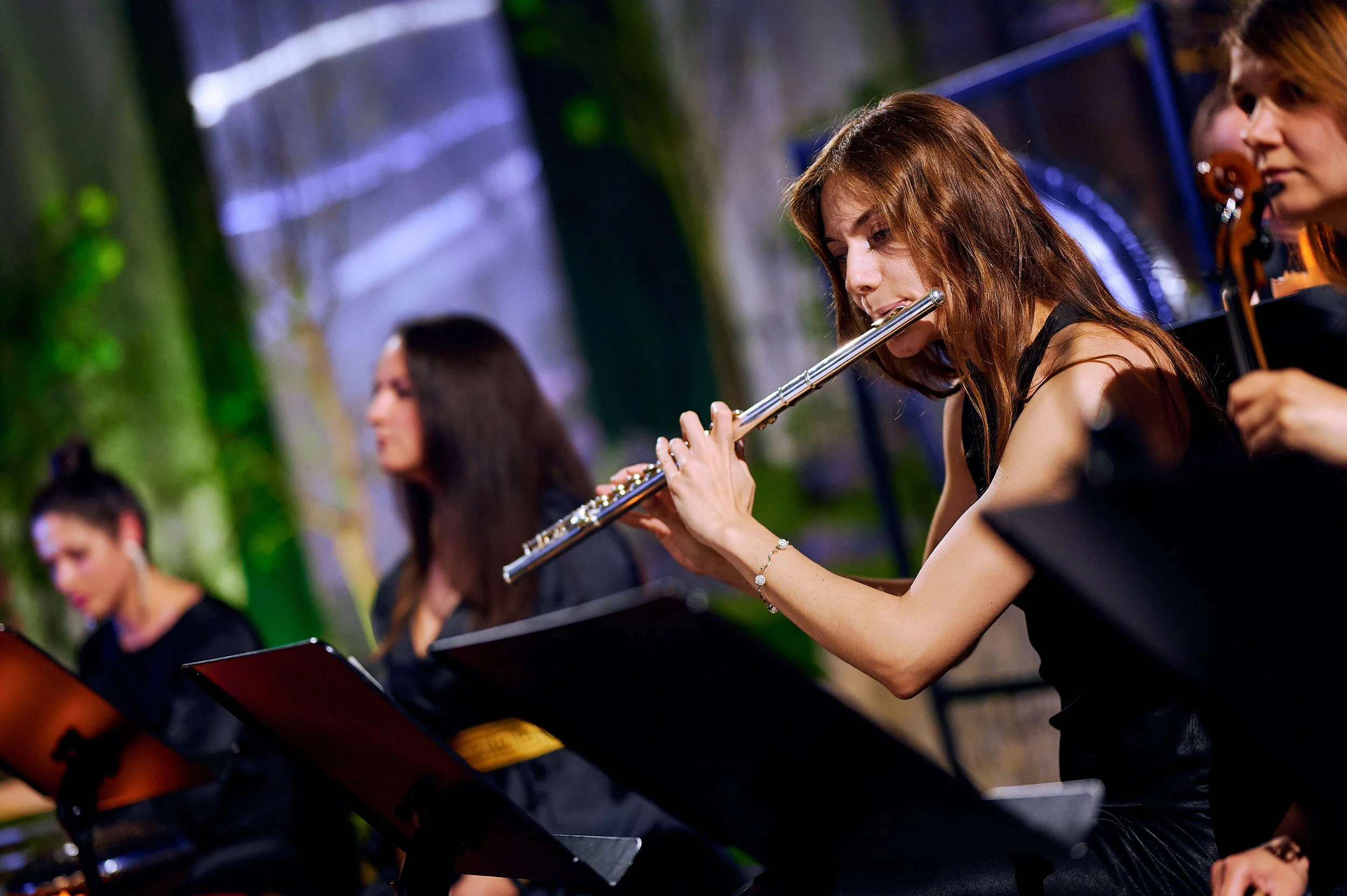Women musicians playing instruments on stage during an outdoor concert at night.