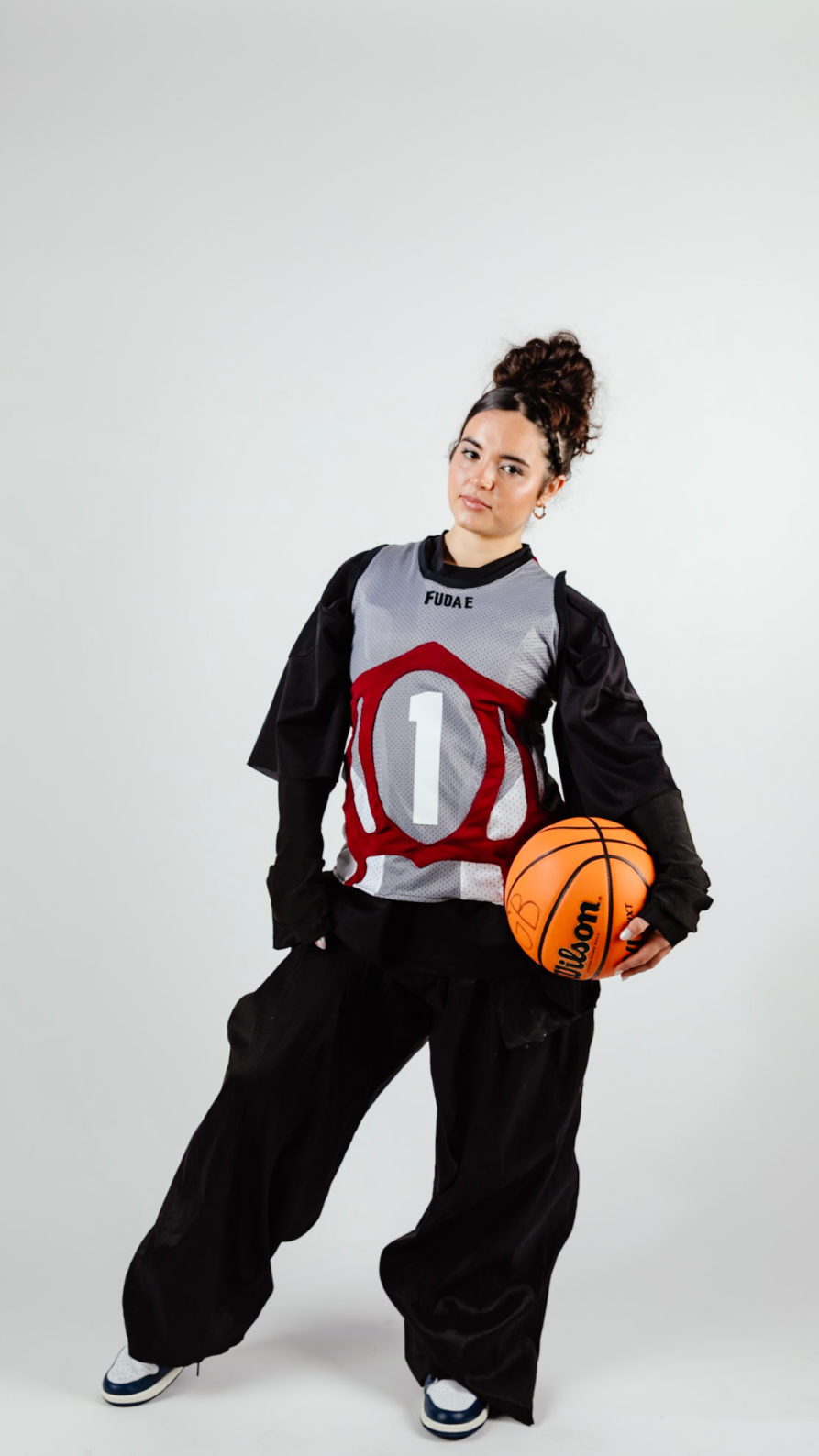 A young woman in basketball attire holding an orange Wilson basketball, standing against a plain background.