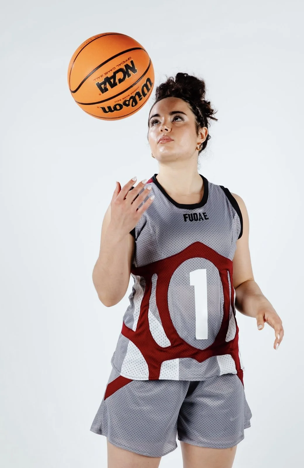 A female basketball player in a gray and red uniform with the number 1, spinning a Wilson basketball in front of a white background.