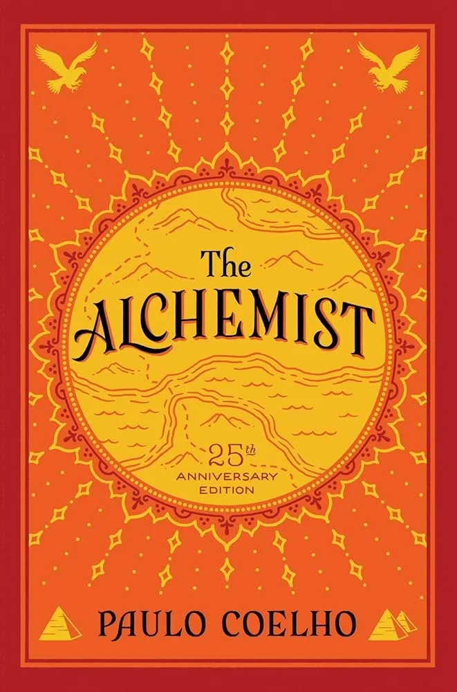 Book cover of 'The Alchemist' by Paulo Coelho, 25th anniversary edition, with a yellow sun and mountain landscape, surrounded by decorative patterns, set against an orange and red background.