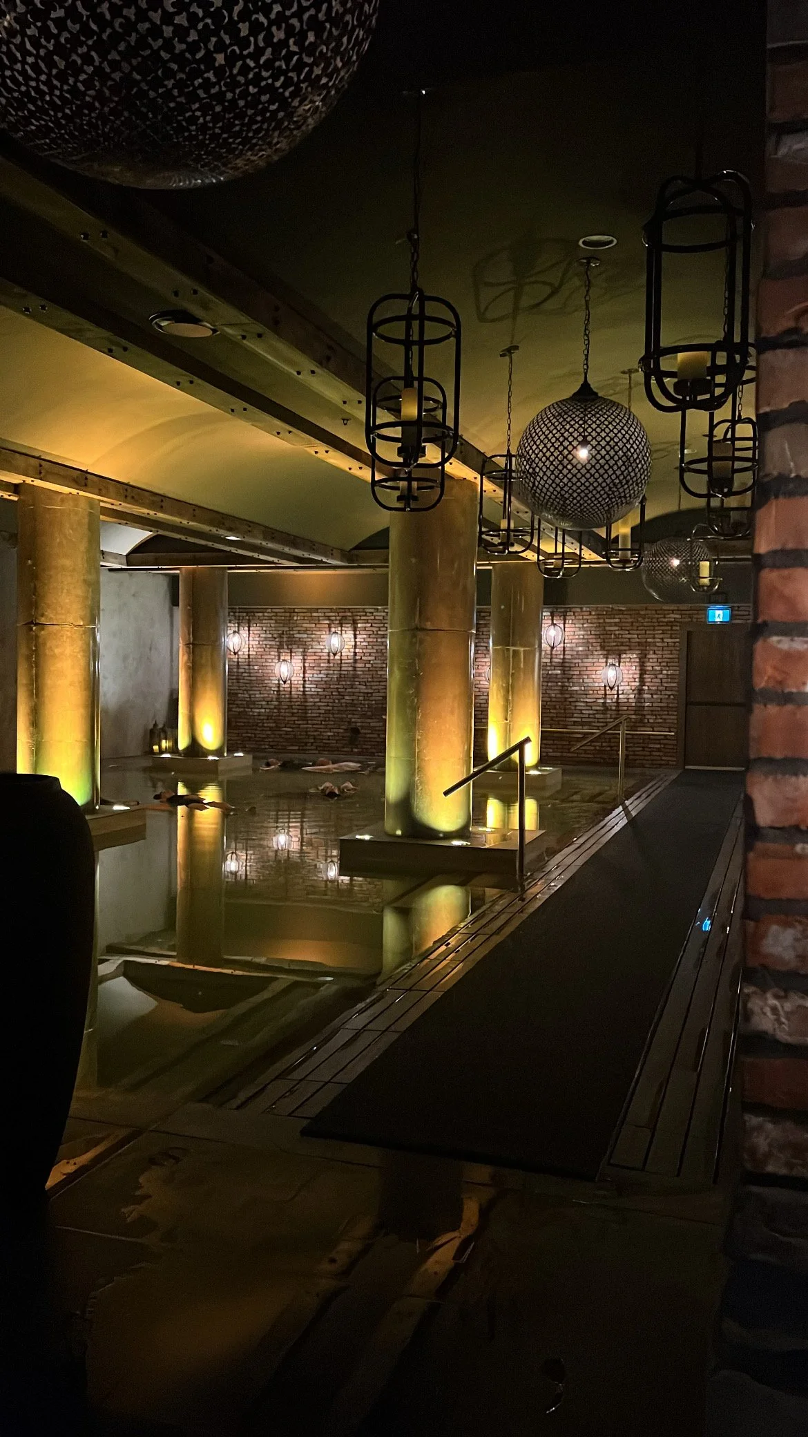Indoor spa with a pool, large gold columns, brick wall, and decorative suspended lanterns