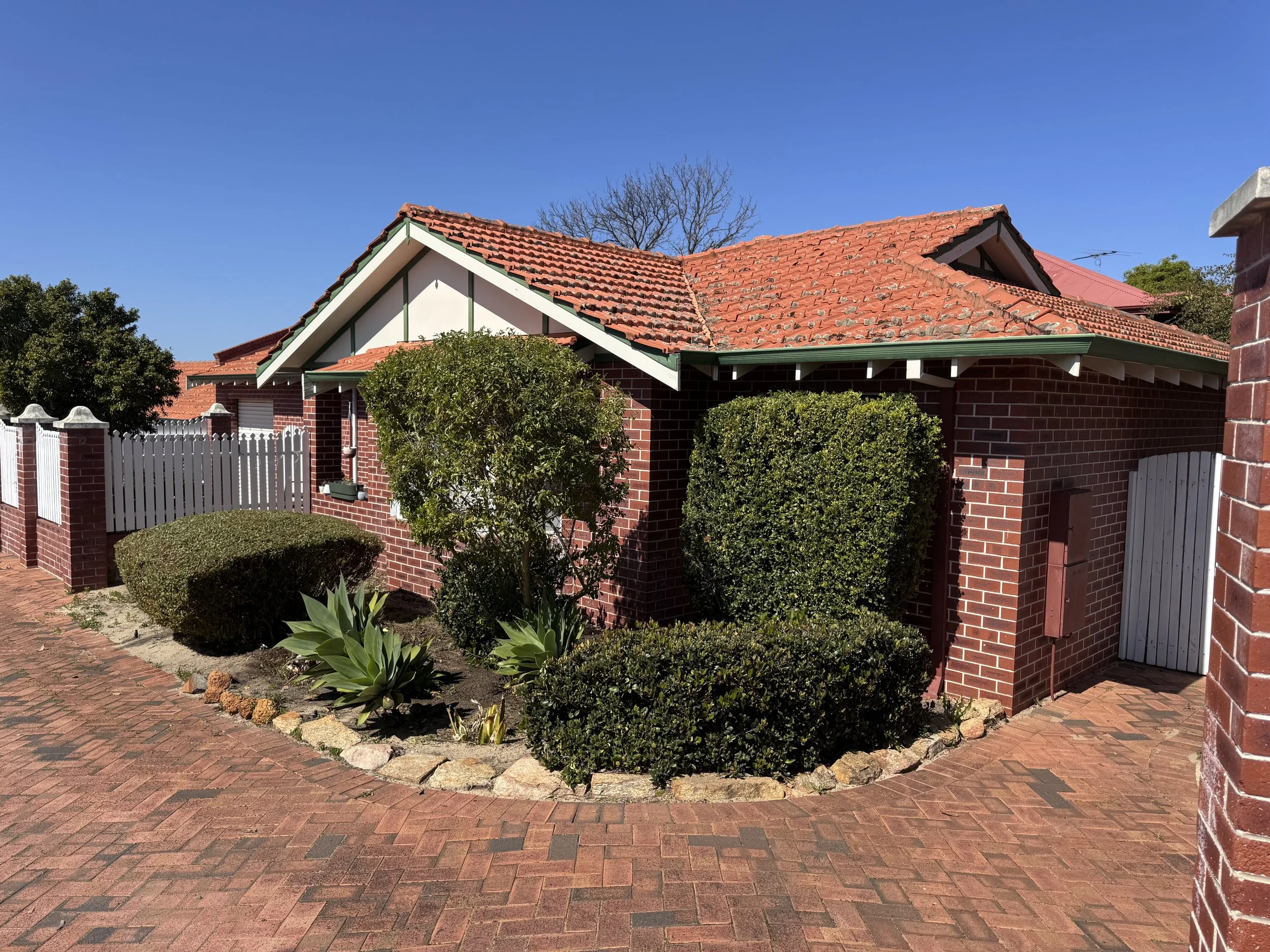 Modern wooden building with large glass window, set in a mountainous landscape with green and brown terrain and rugged peaks in the background.