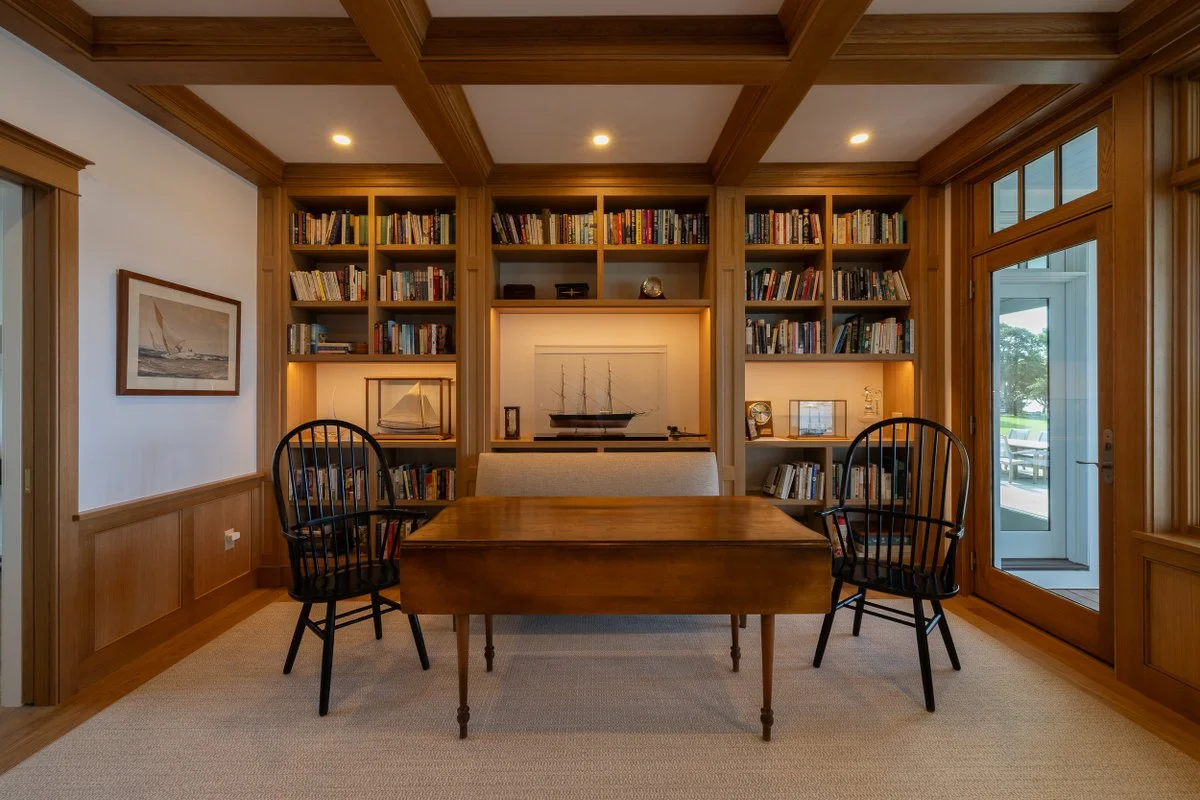 A cozy library room with wooden bookshelves filled with books, a wooden table with three black chairs, and a doorway to an outdoor patio.