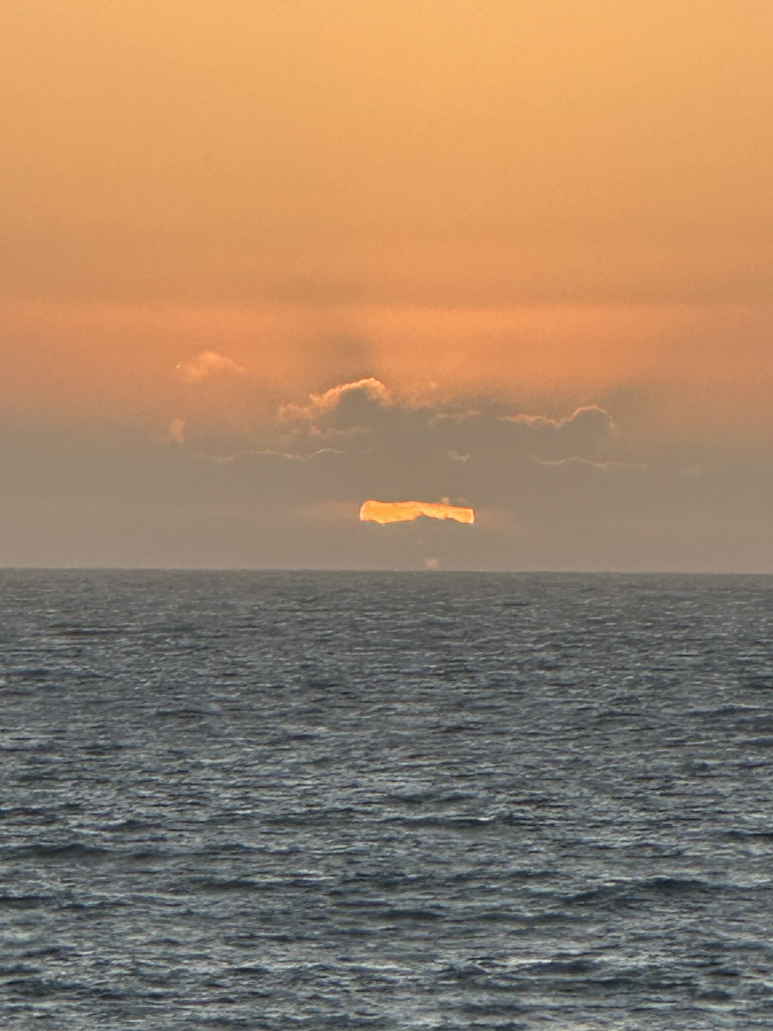 Sunset over the ocean with clouds and a bright orange glow near the horizon.