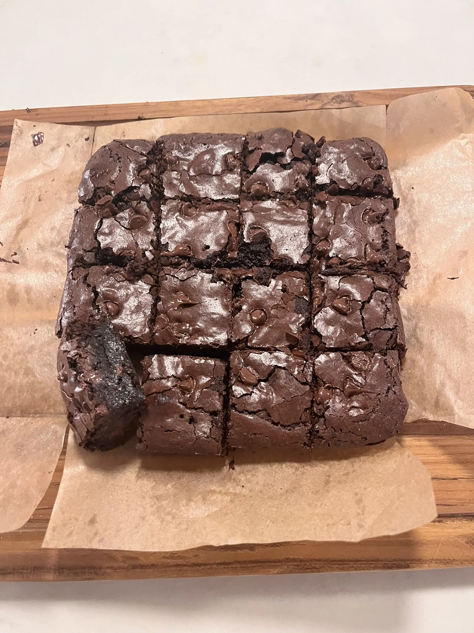A wooden tray with a lined sheet of parchment paper holding a large batch of cut, homemade double chocolate brownies with chocolate chips.