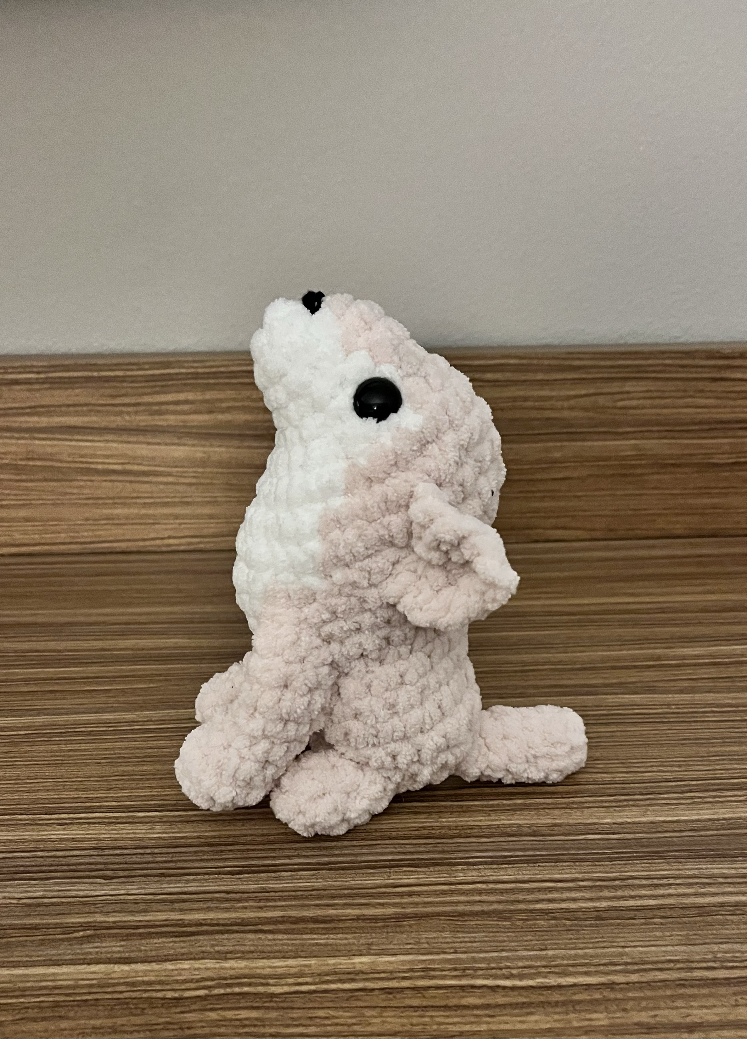 A plush toy in the shape of a dog sitting on a wooden surface against a light-colored wall.