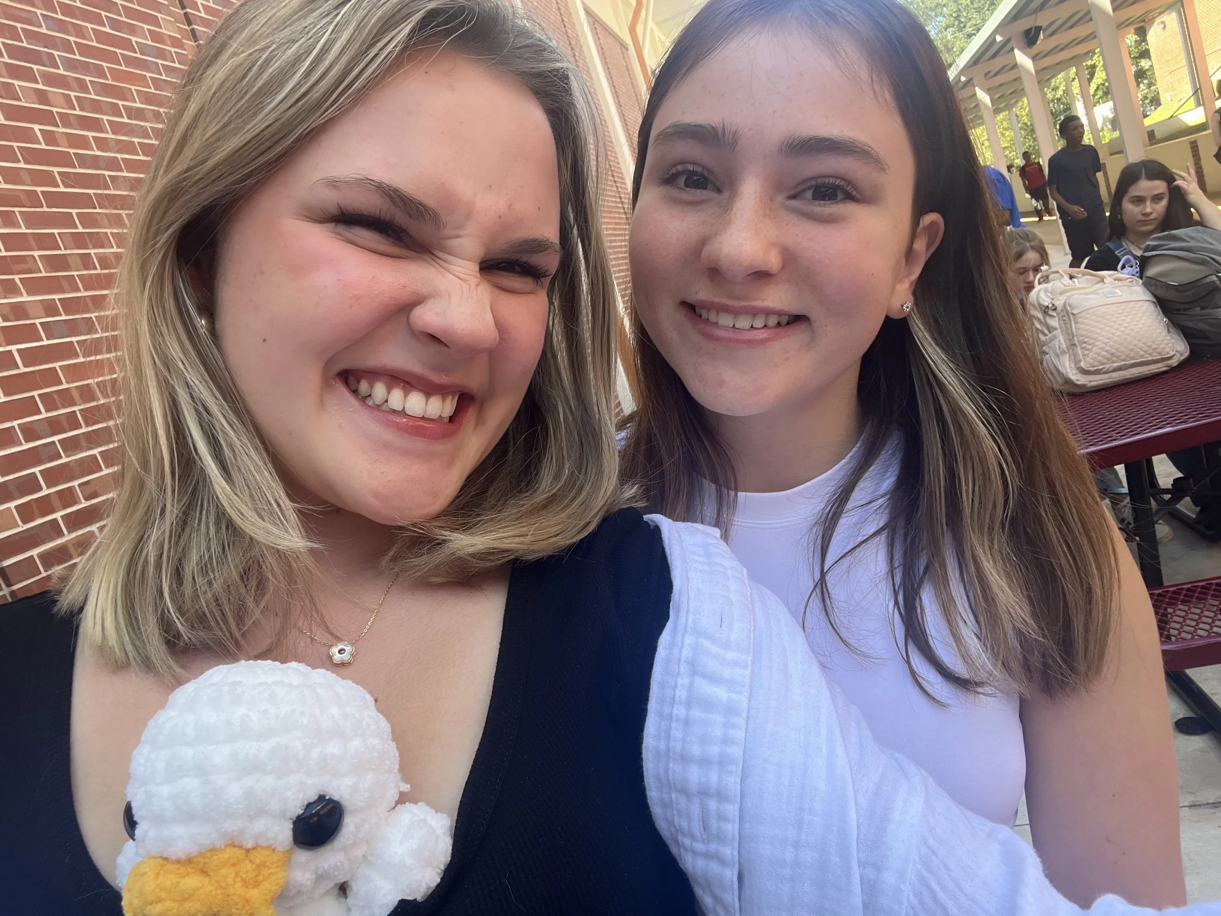Two young women taking a selfie at school, one holding an adorable plush duck toy