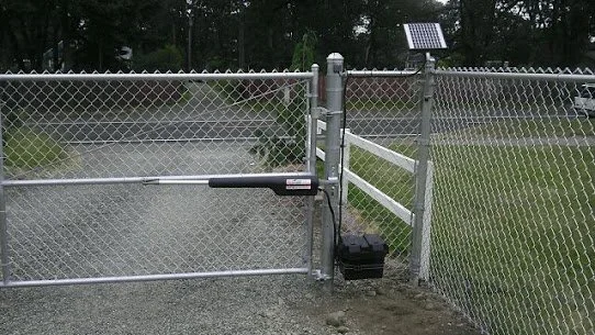 Chain-link fence with electric gate and solar panel on top, set in a grassy outdoor area