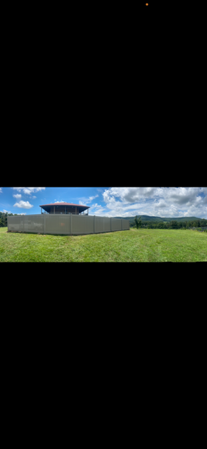 A round building with a glass exterior on a hill, surrounded by a grassy field under a blue sky with scattered clouds.