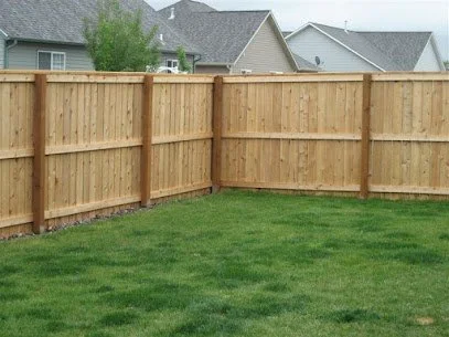 A backyard with a green lawn and a new wooden privacy fence, with neighboring houses visible in the background.
