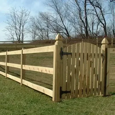 Wooden fence with a gate in a grassy yard, trees in the background.