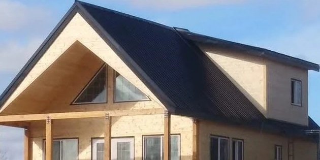 A house under construction with a steeply pitched roof, exposed wooden beams, and large windows, set against a blue sky.