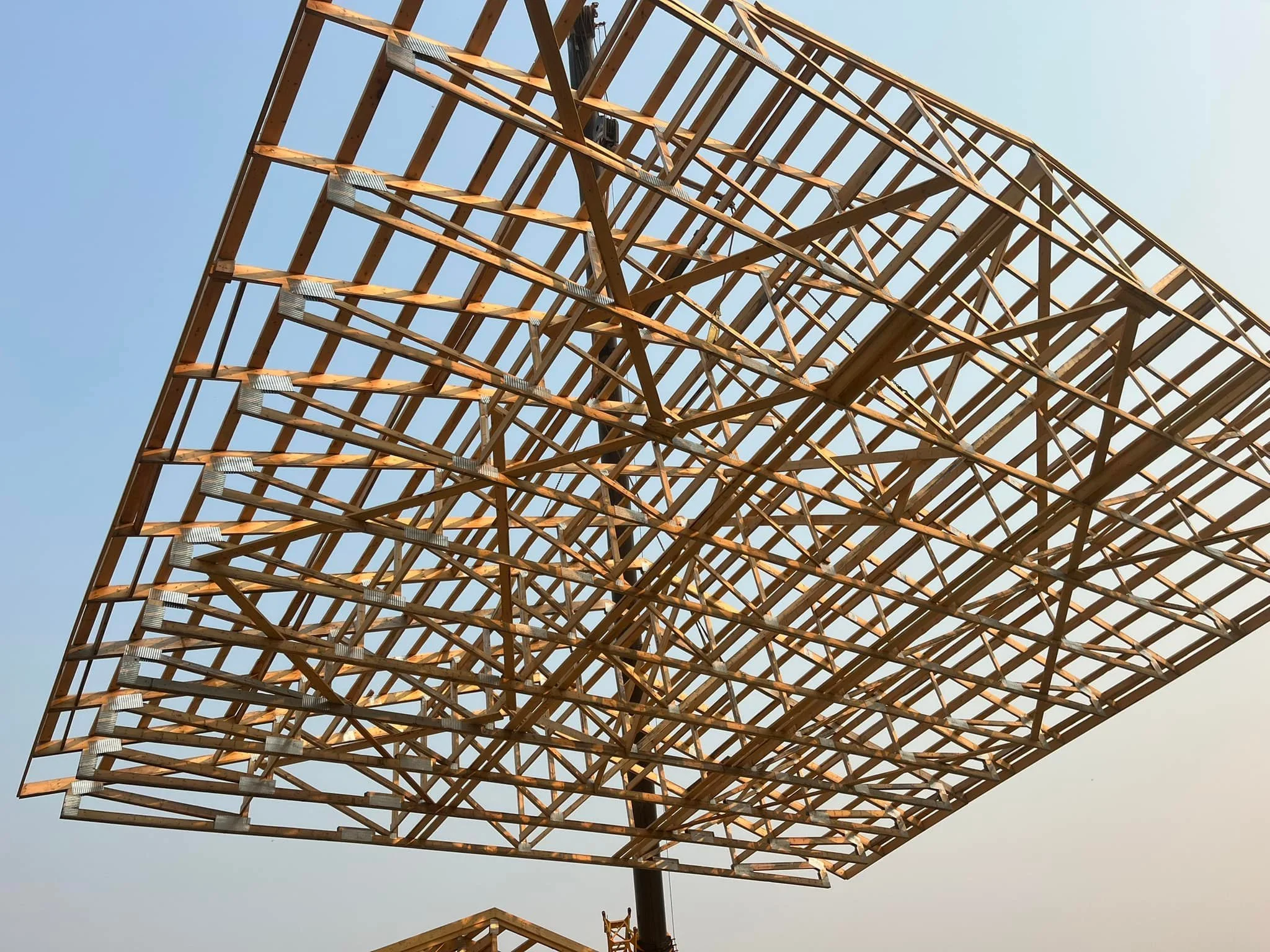 A large metal framework structure under construction, viewed from below against a clear sky.