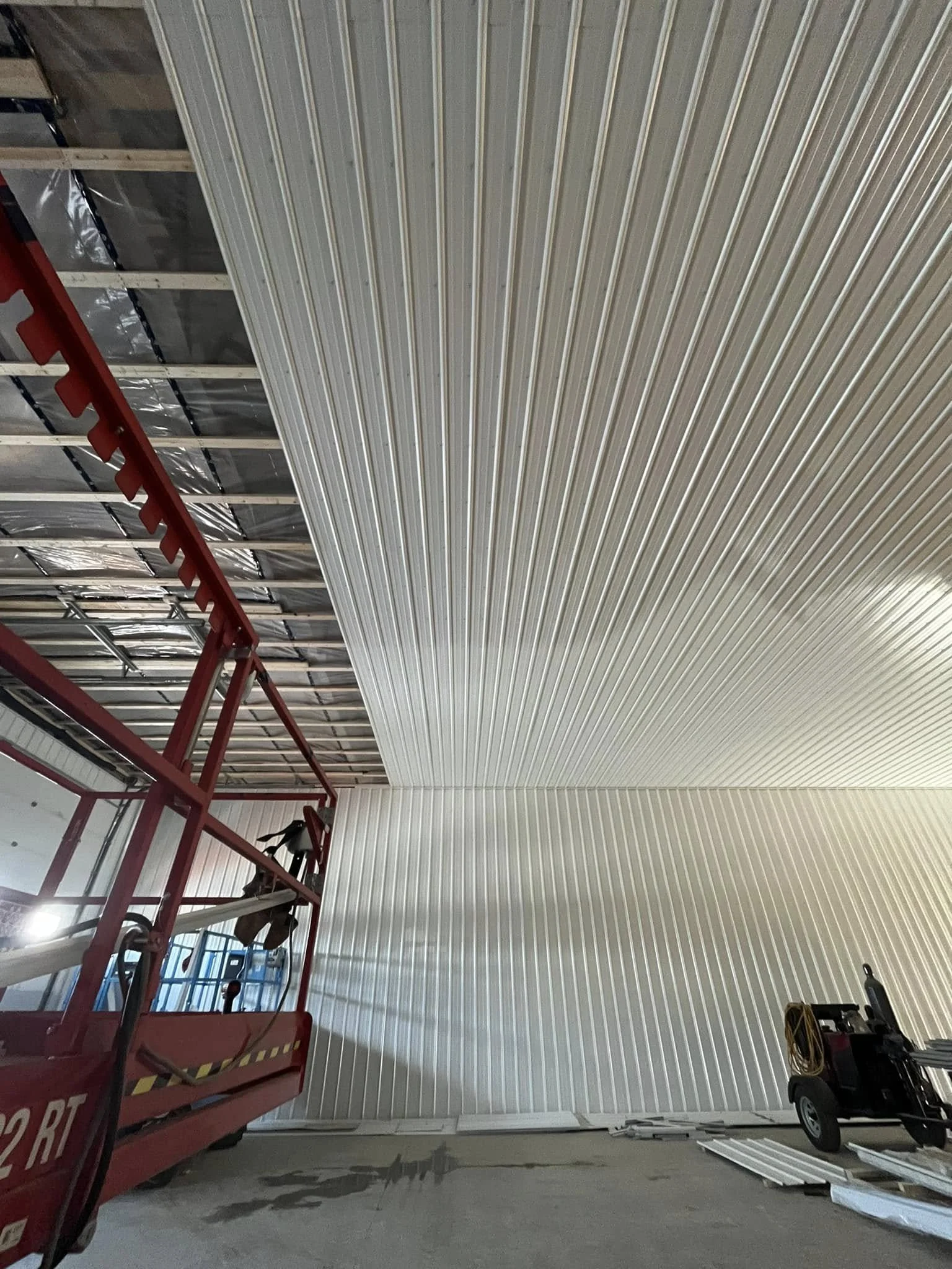 Construction site with metal wall panels, a red lift, and construction equipment.