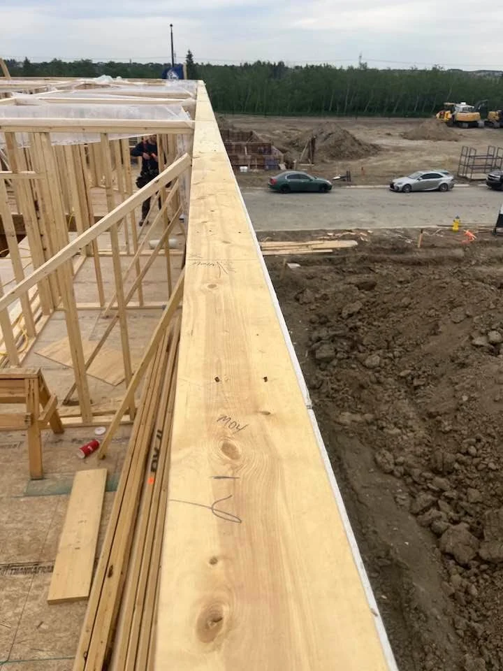 Construction site with wooden framing on a building under construction, with dirt and vehicles visible in the background.