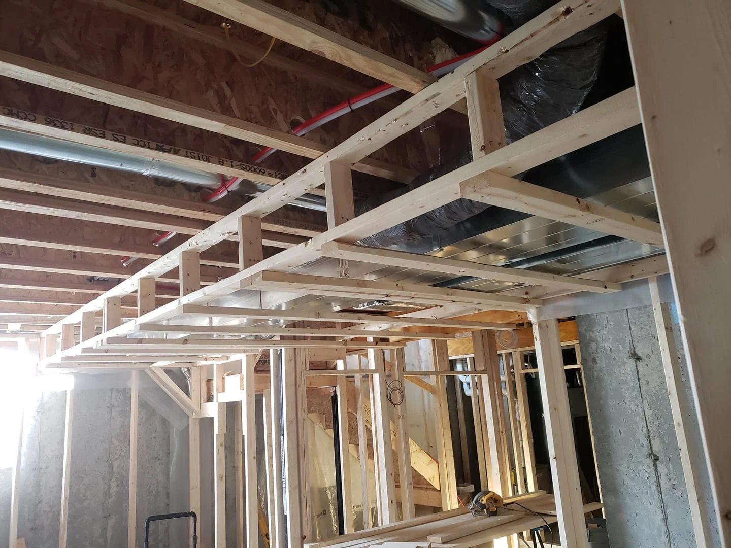 Wood framing for a building under construction, showing ceiling joists, ductwork, and pipes.