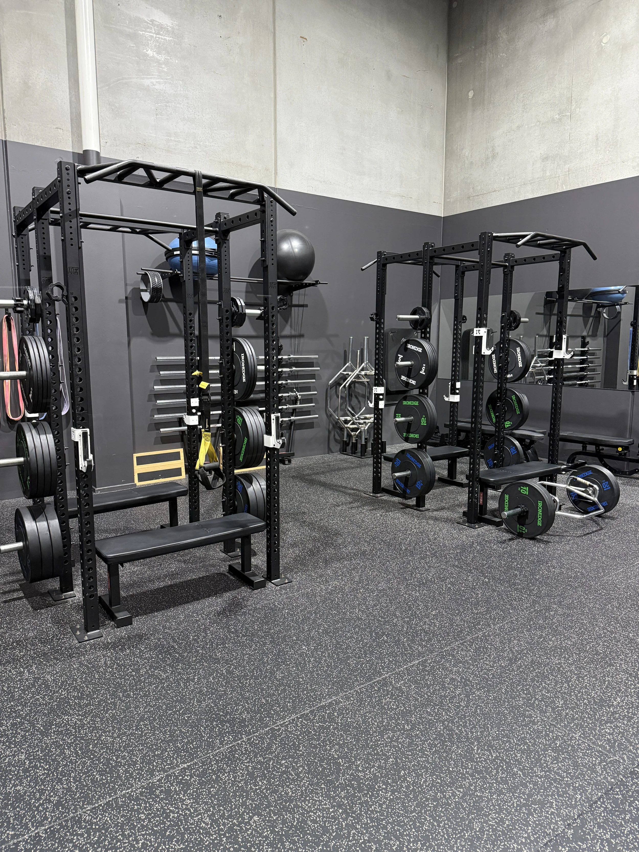 Workout gym with black squat racks, weight plates, a large exercise ball, and functional training equipment against gray walls.