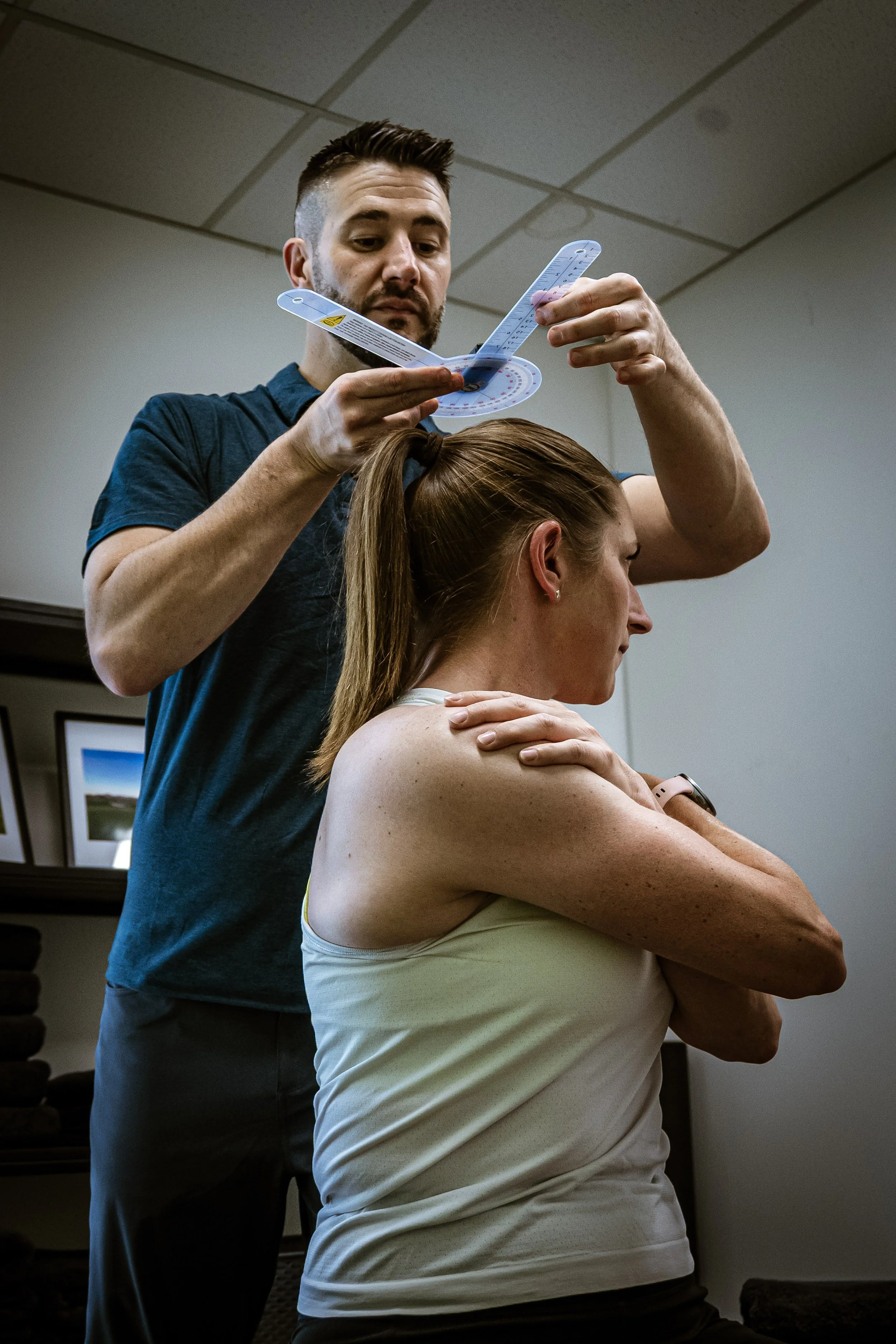 A man using a protractor and rulers on a woman's shoulder and neck in a clinical setting.