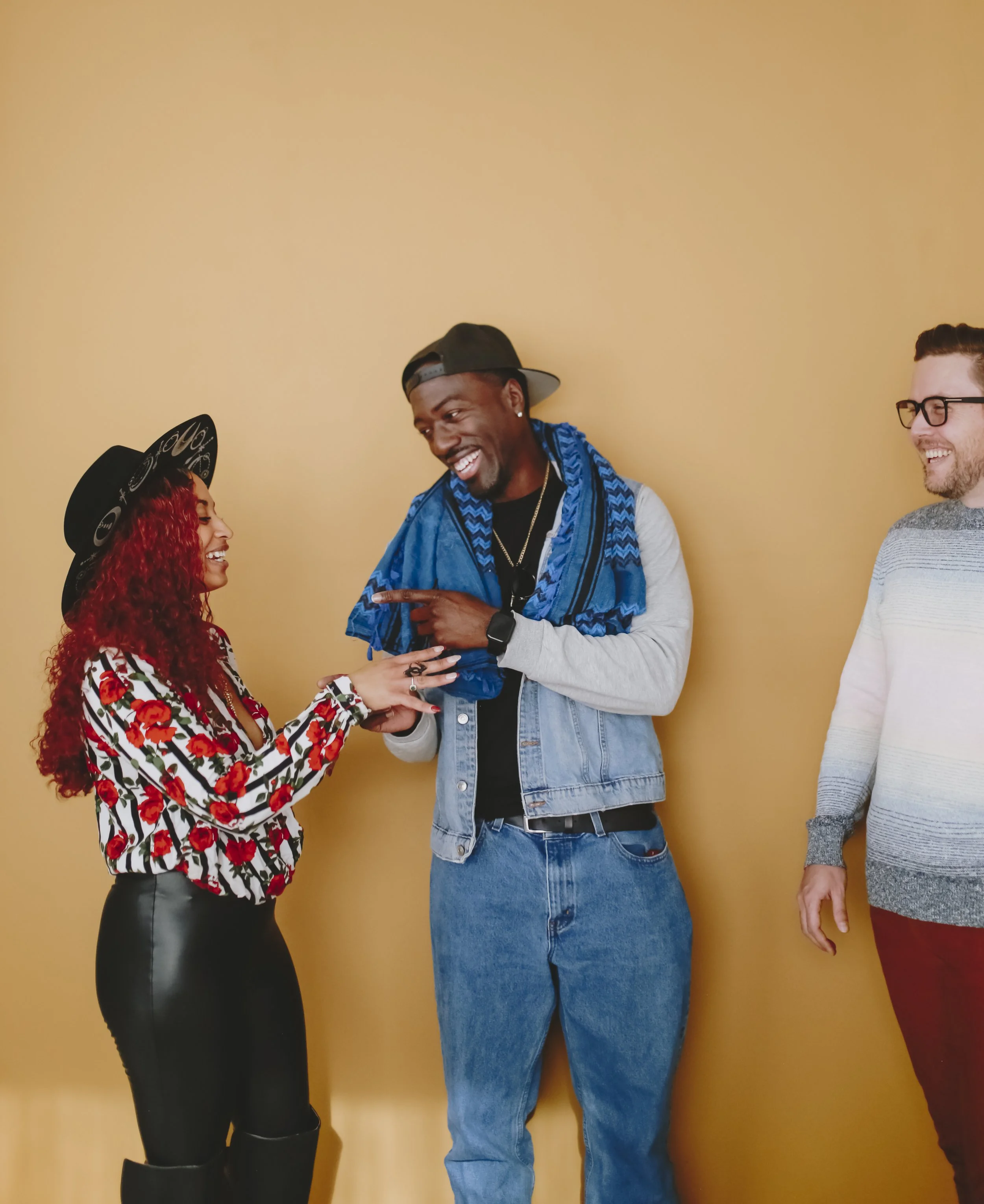 Three friends laughing and chatting against a plain yellow wall.