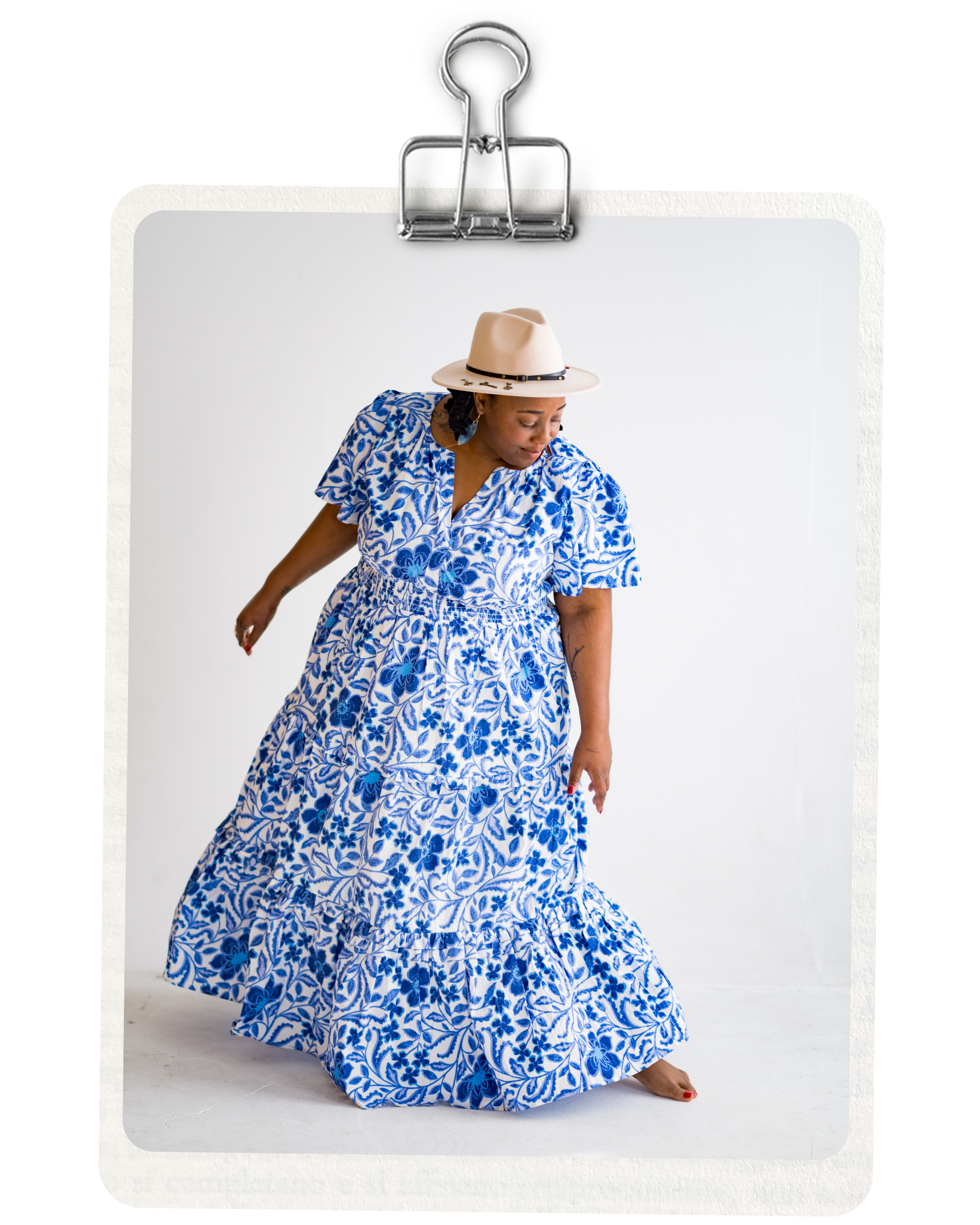 Nyasha Williams in a blue and white floral dress and beige hat dancing against a plain white background.