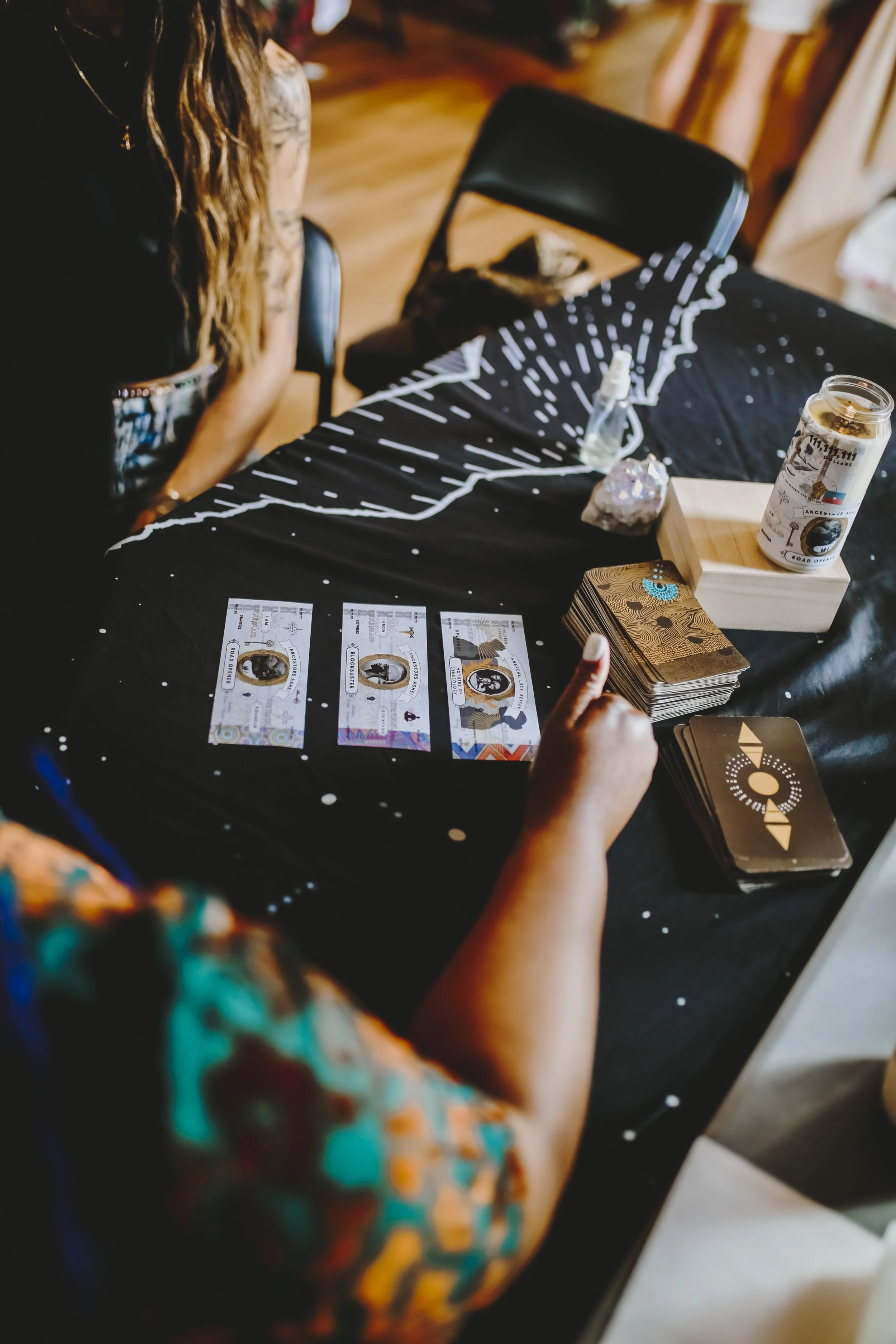 Person giving a thumbs up next to a tarot card reading setup on a black tablecloth with a celestial design, money, and tarot cards.