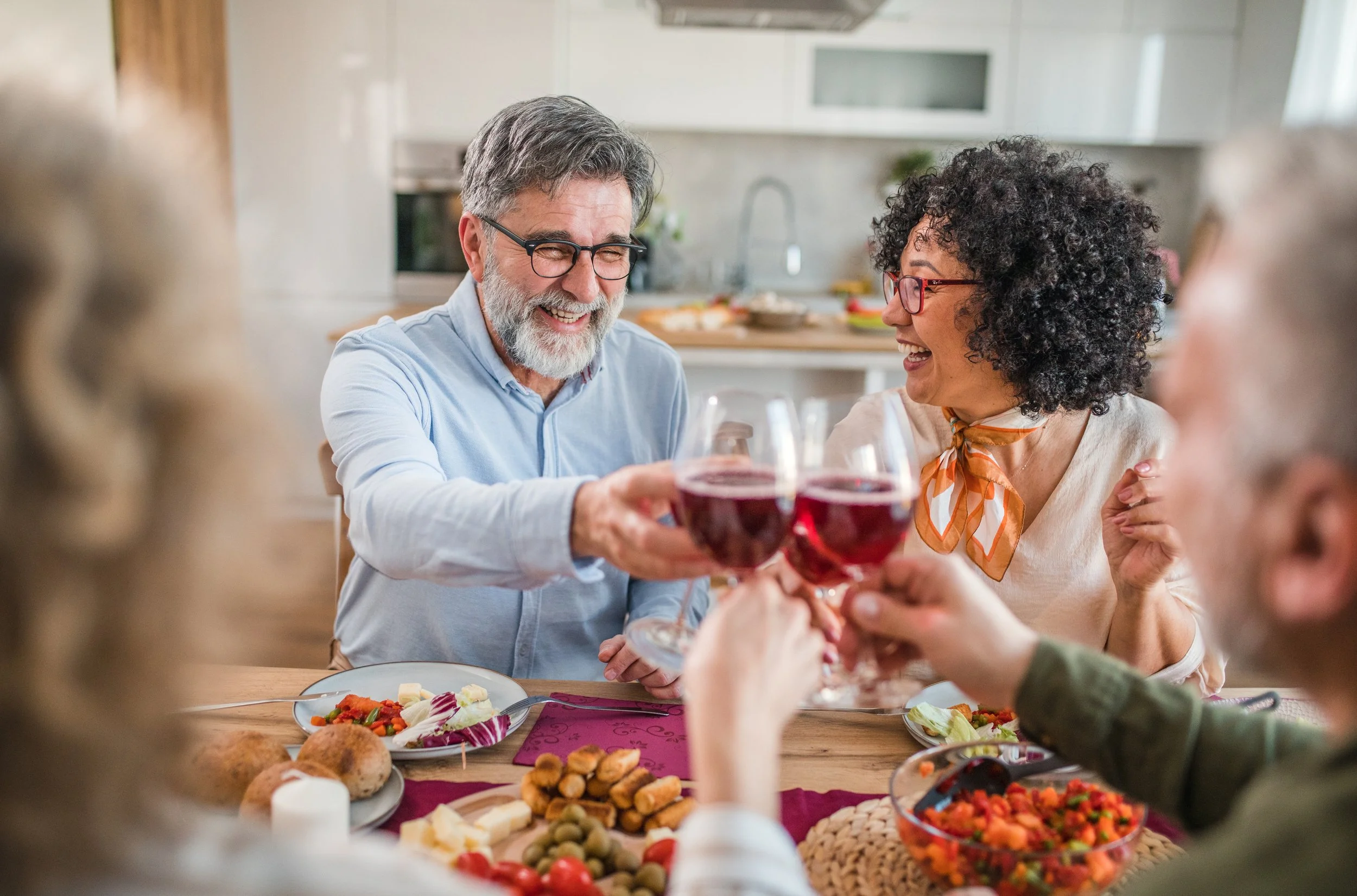 Grupo de personas mayores brindando con copas de vino en una comida compartida, en una cocina moderna.