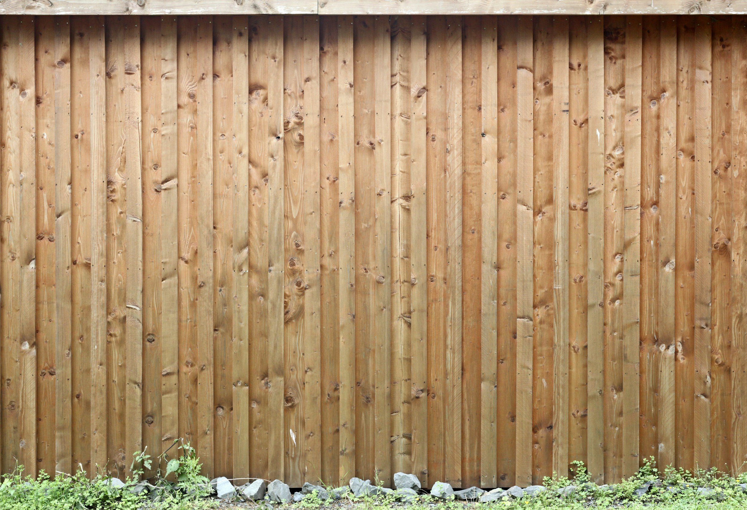 wooden privacy fence with a row of small rocks and green plants at the base.