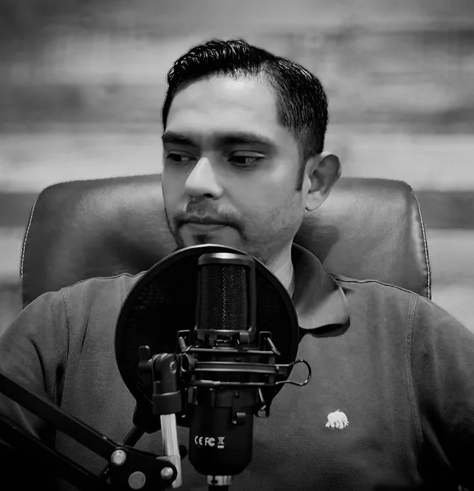 Hombre sentado frente a un micrófono con filtro, en un estudio de grabación, en blanco y negro.