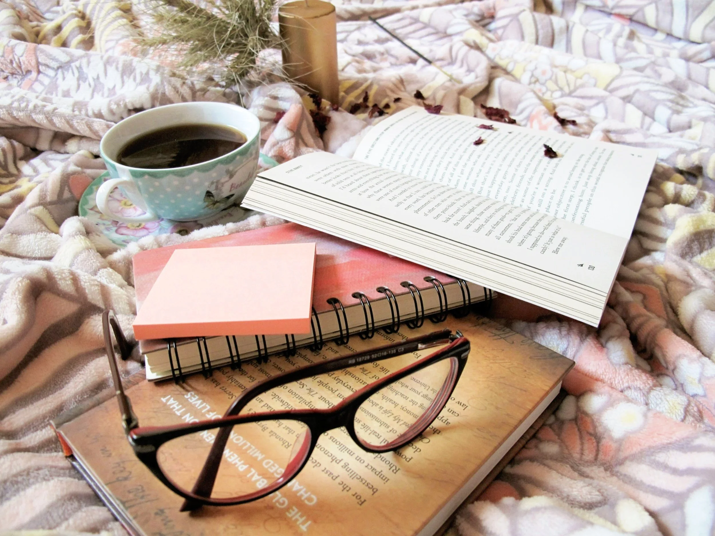 Open book with coffee, notes, and glasses in a quiet reading setting.