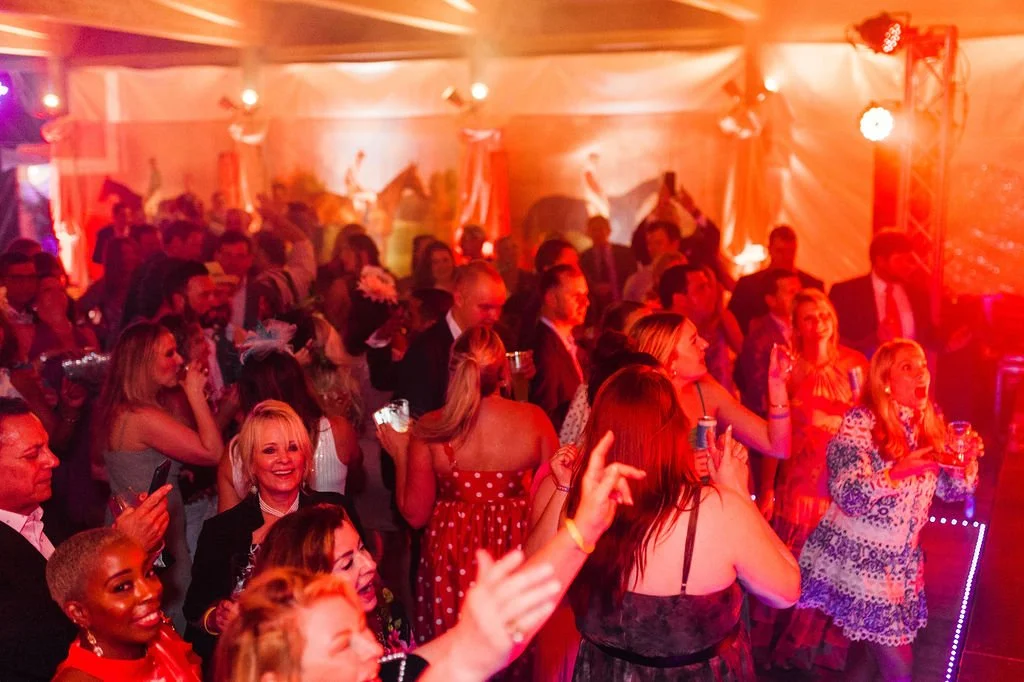 The Silks Bash Gala with many people dancing and socializing inside a brightly lit venue with red lighting and cowboy-themed decorations.