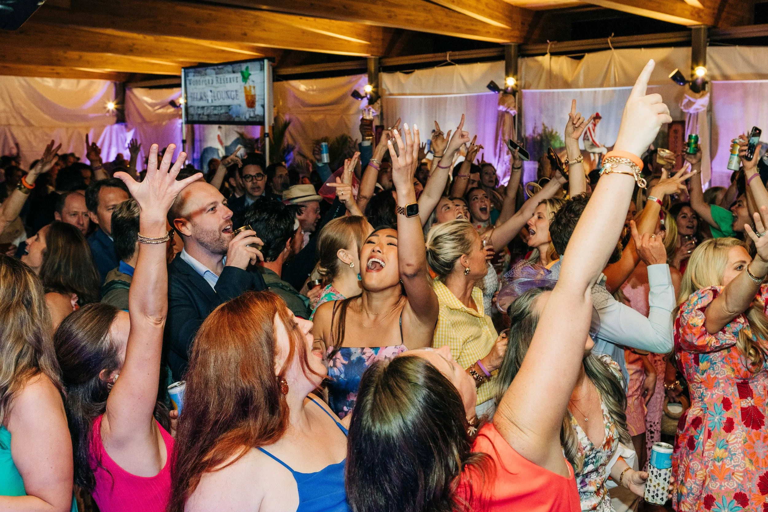 Crowd of people at a the Silks Bash Gala, many with hands raised, smiling and enjoying the event, with lights and decorations in the background.