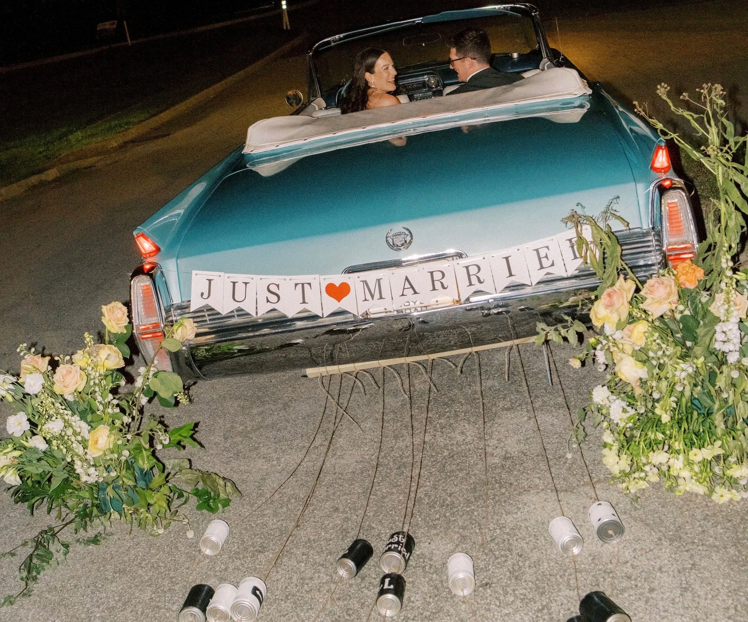 Charlene, a 1964 Cadillac Eldorado convertible in Turino Turquoise, decorated for a wedding with a JUST MARRIED sign on the rear, cans attached to the bumper and floral arrangements placed on either side of the vehicle.