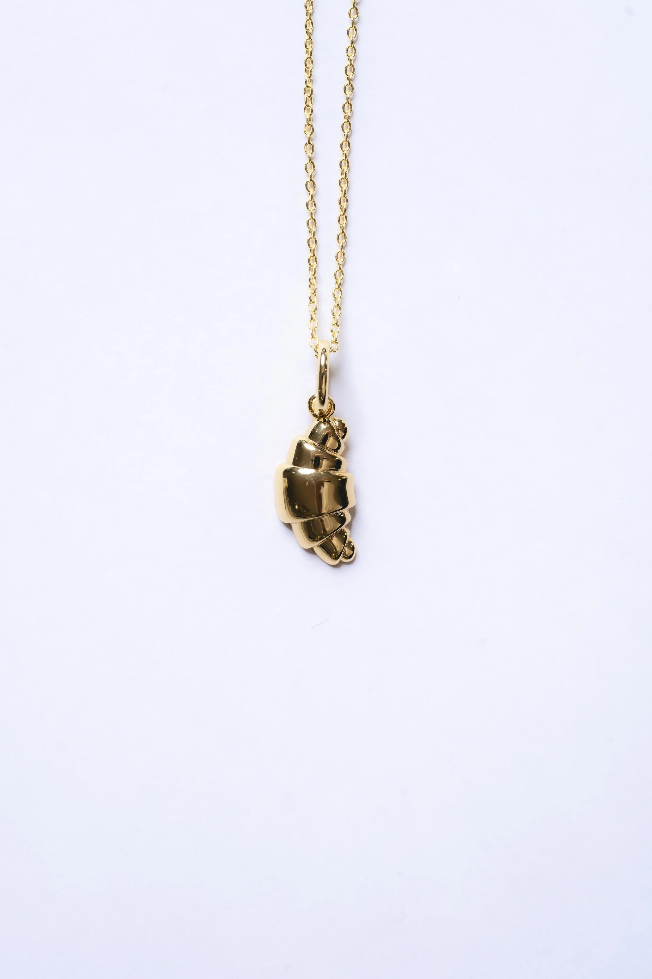 Gold necklace with a pendant shaped like a closed fist, hanging against a white background.