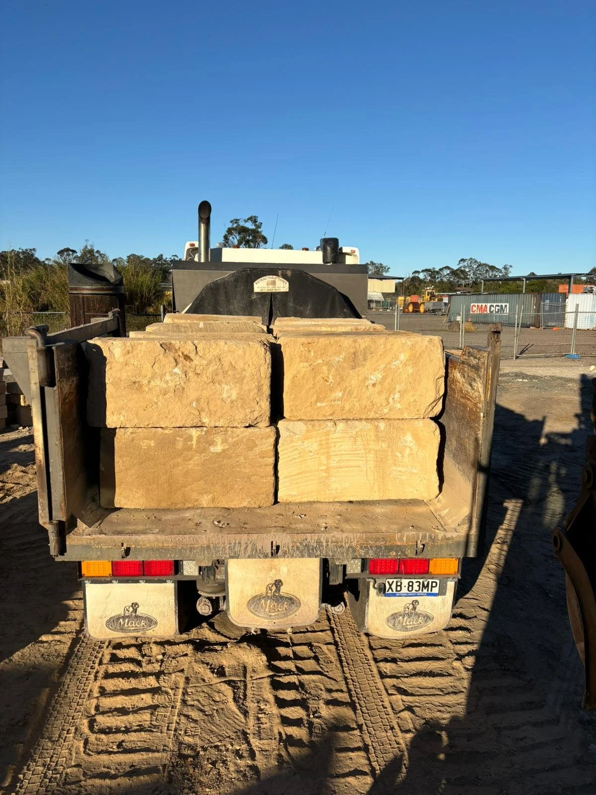 Back view of a small utility vehicle carrying large sandstone blocks on a construction site.