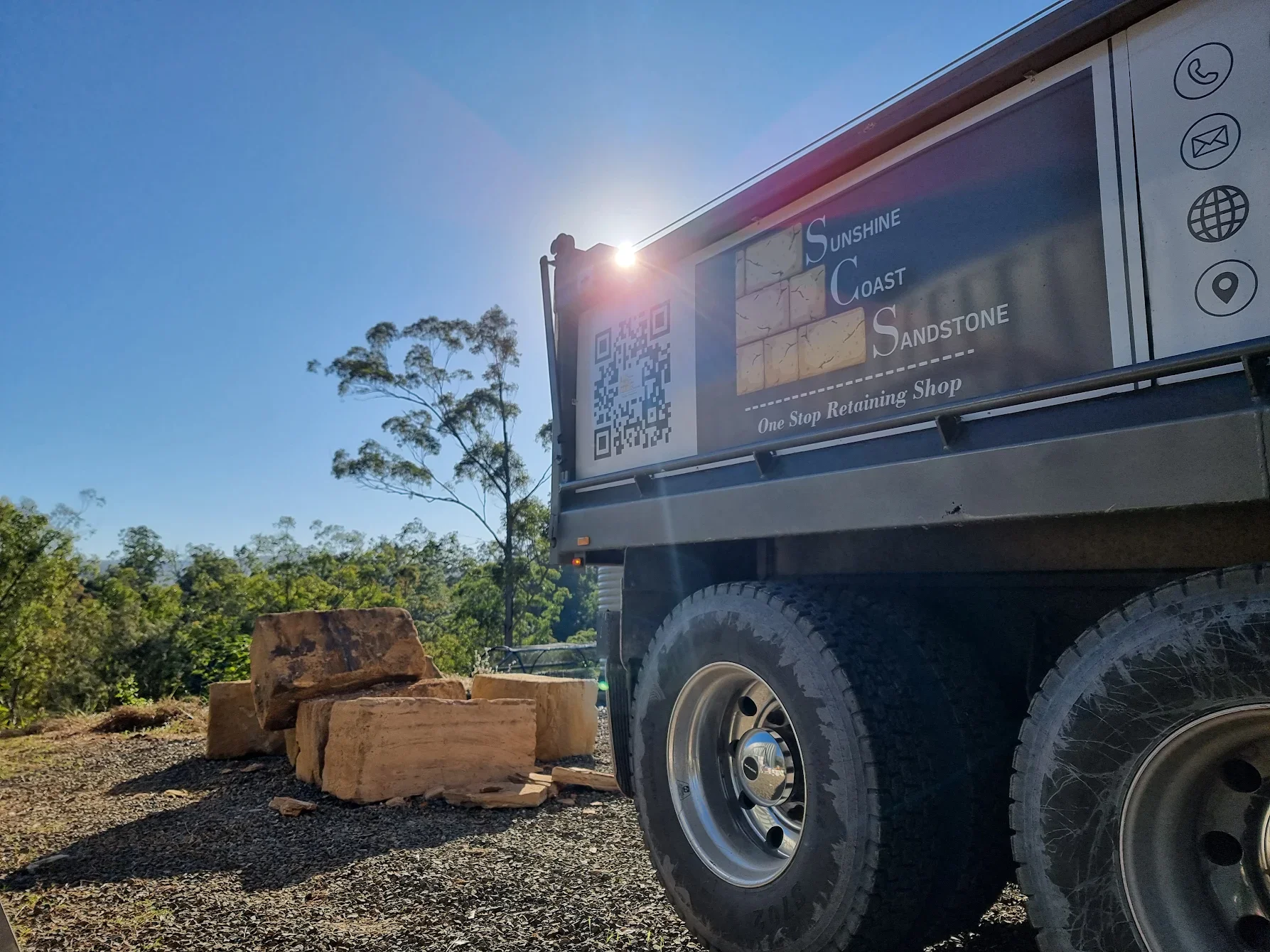 Sunshine Coast Sandstone image of the company tipper truck parked outdoors near piles of sandstone with trees and clear blue sky in the background.