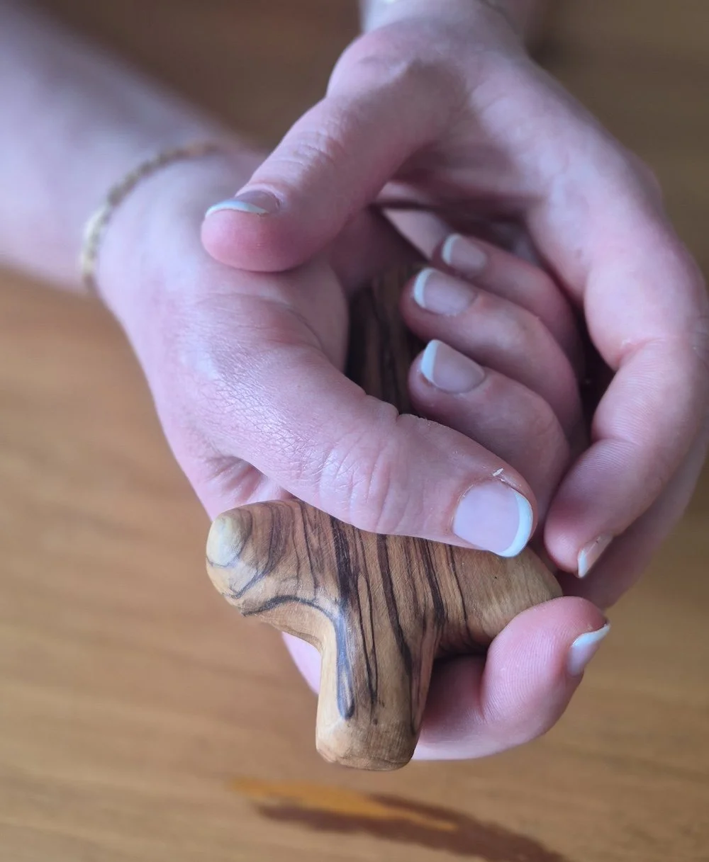 A person's hands with a holding cross, with a visible manicure with white tips and a gold bracelet.
