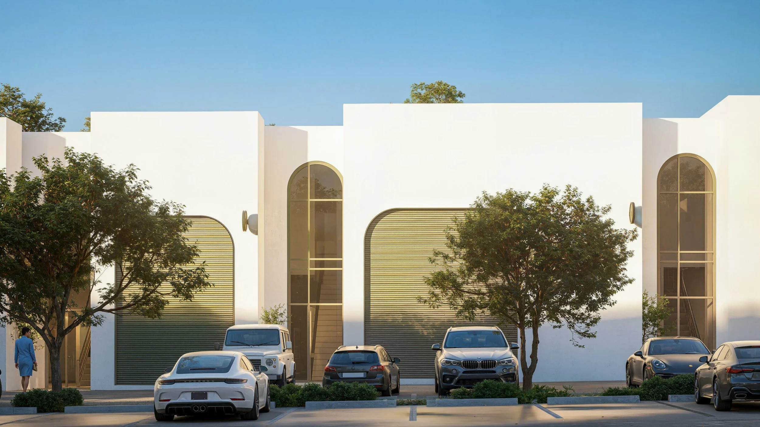 Modern white building with large arched windows, parked cars in front, trees, and a clear blue sky.