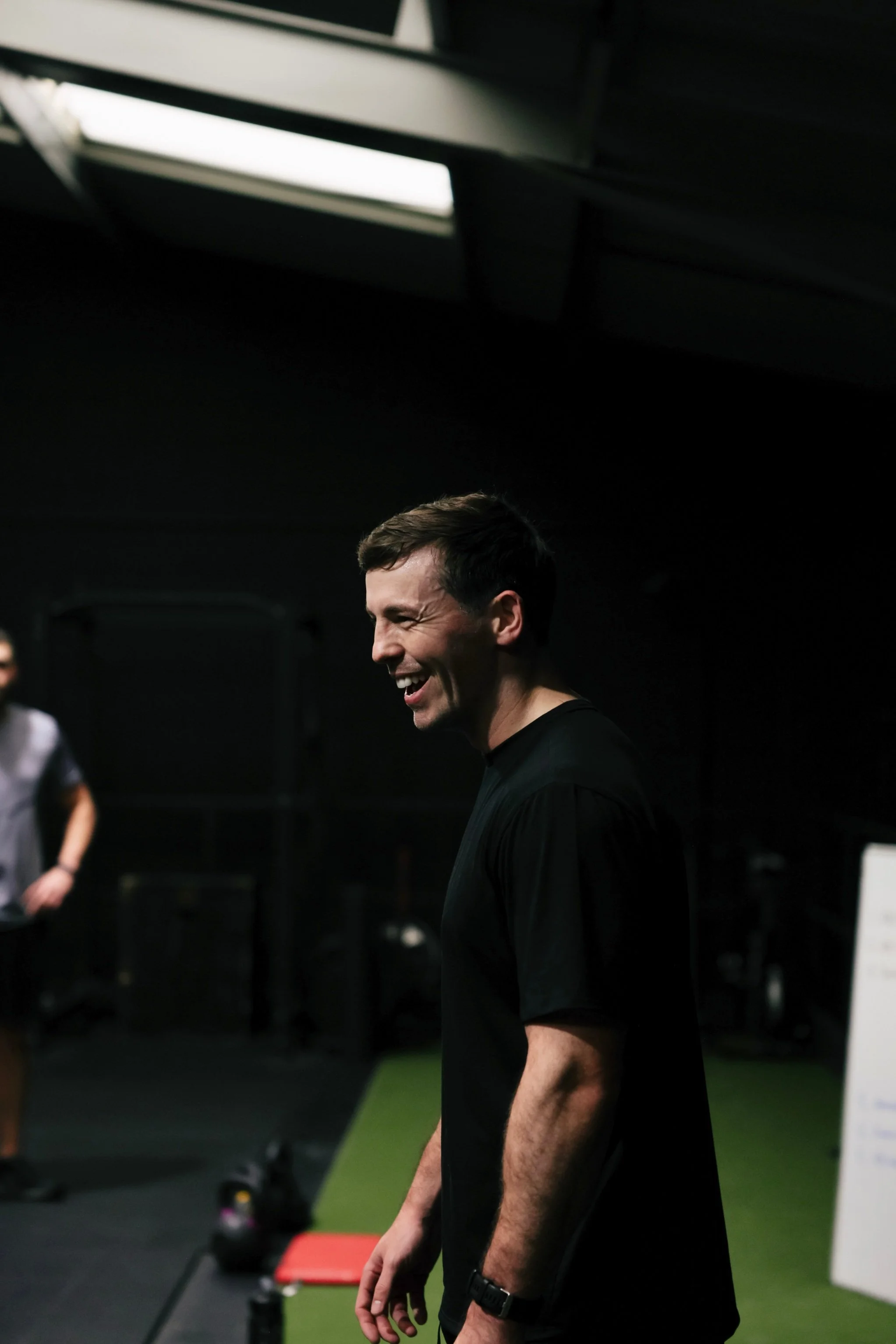Personal trainer smiling and interacting with clients during a strength and conditioning session in a gym.