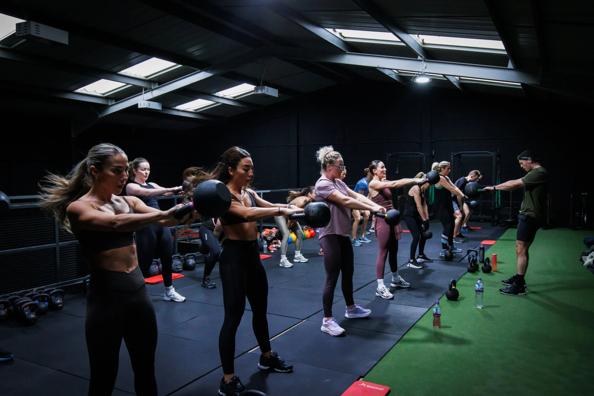 Group fitness class performing kettlebell swings in a gym.