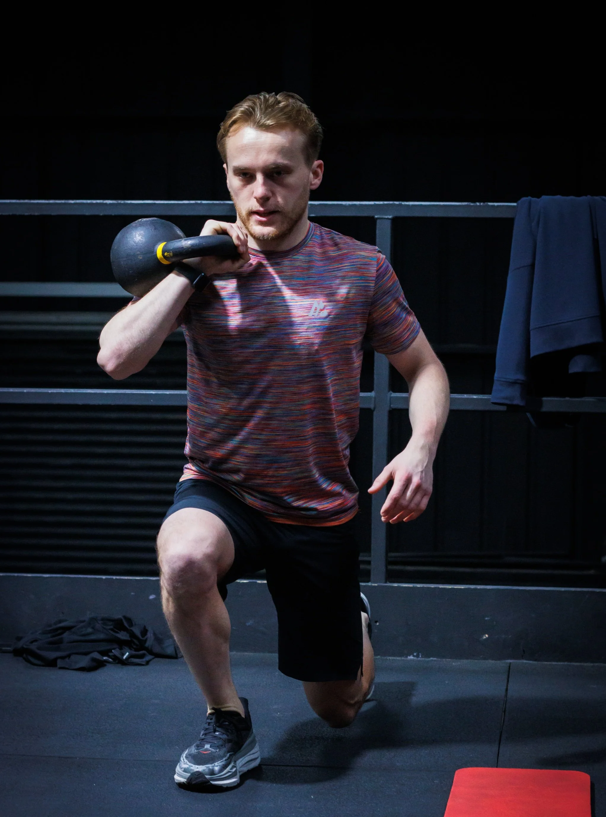 Man performing a kettlebell lunge in a gym, holding the weight at shoulder height while focusing on balance and lower body strength.