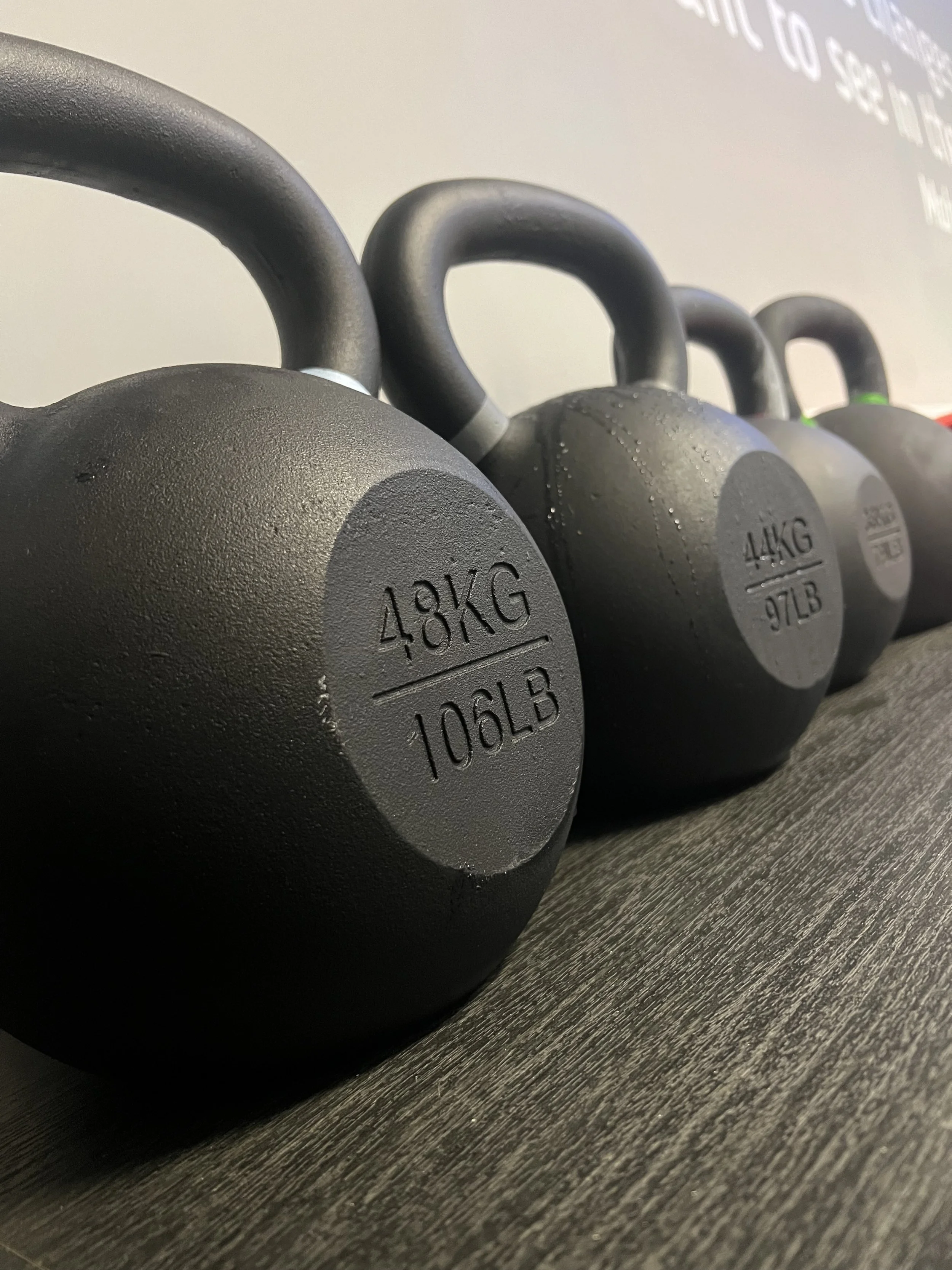 Row of heavy kettlebells lined up on the floor with text reading “Kettlebell Classes.”