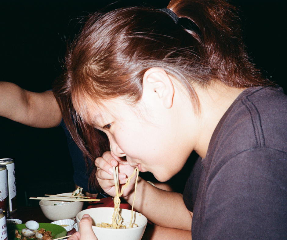 Person eating noodles with chopsticks at a table with other dishes.